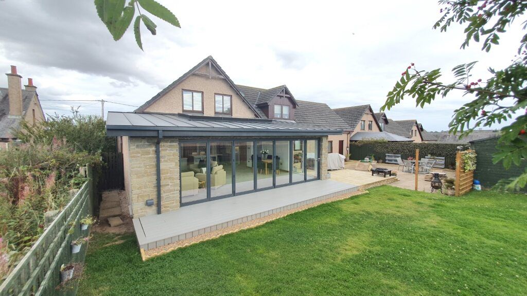 Modern house extension with glass doors and a patio in a green backyard.