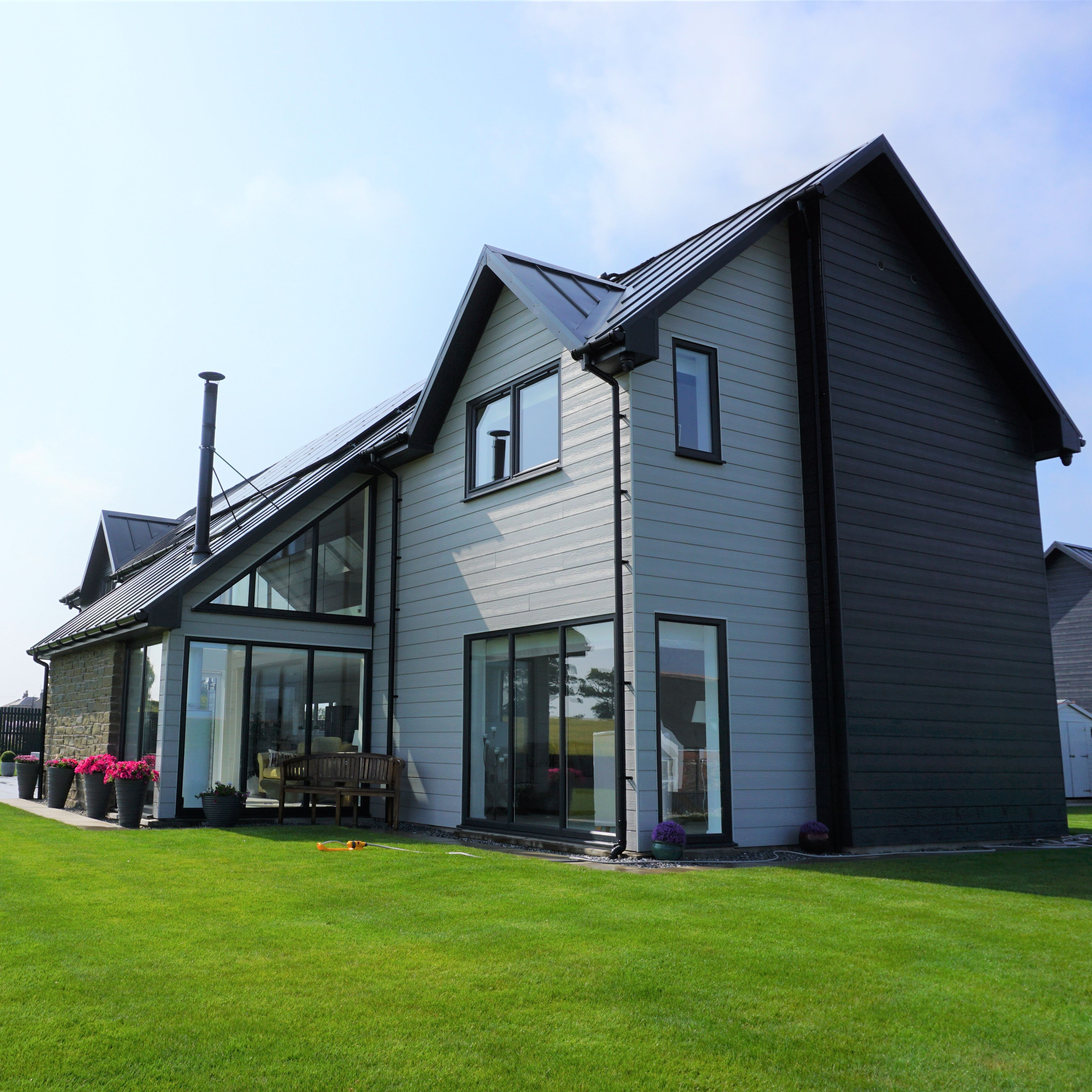 Modern two-story house with large windows, grey siding, and a well-kept lawn.