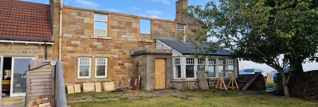 Old stone house with partially boarded windows and missing roof section.