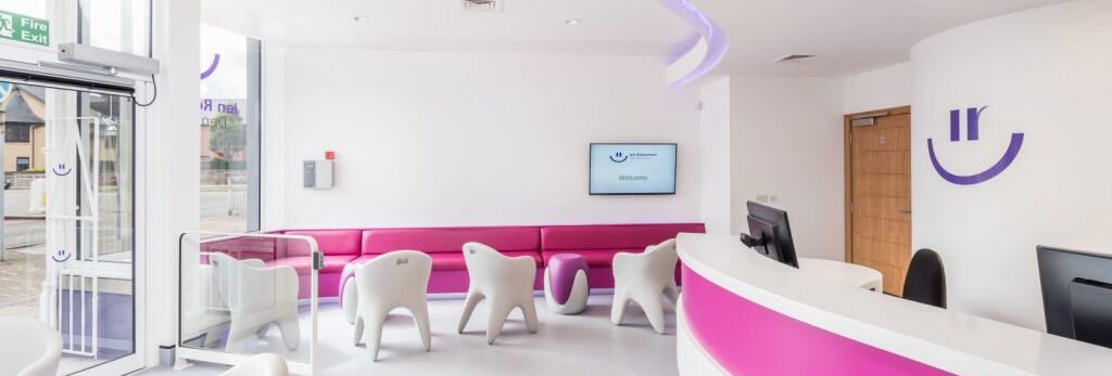 Modern dental or medical clinic waiting area with pink and white decor, curved reception desk, white chairs, and a welcoming atmosphere.