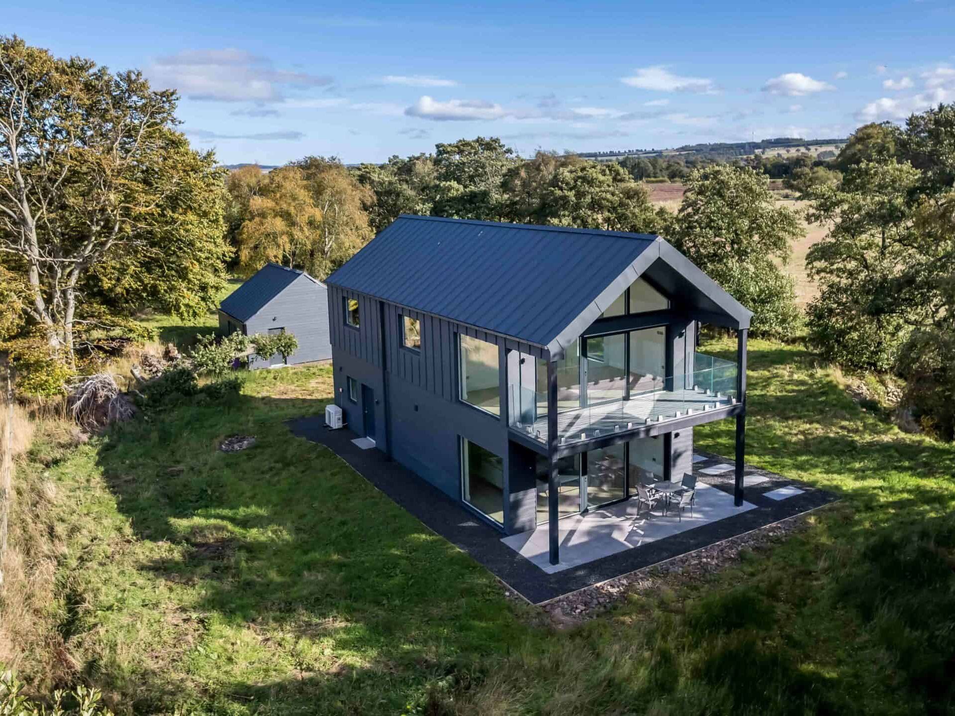 Modern black barn-style house with large windows and balcony in a rural landscape