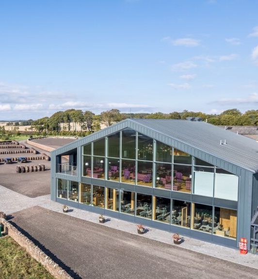 Modern glass-fronted building surrounded by green fields under a blue sky