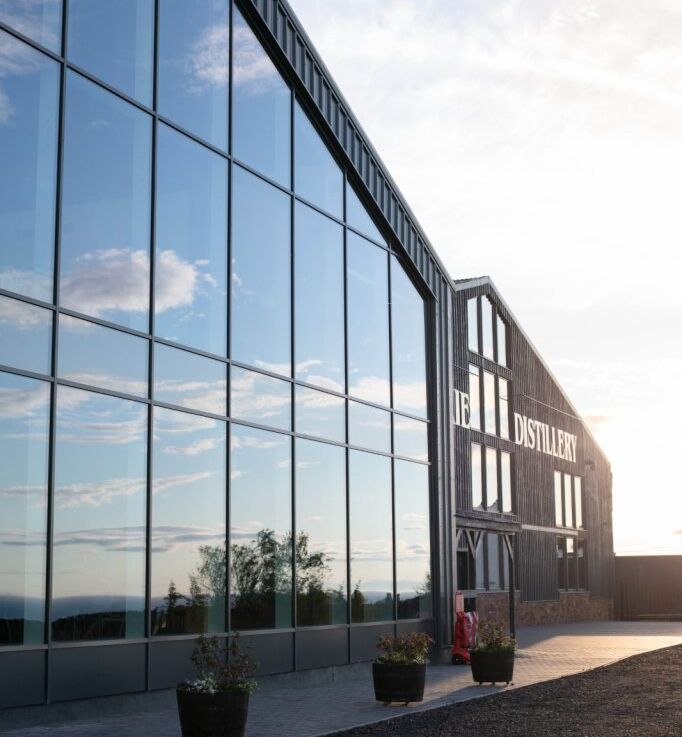Modern distillery building with large glass windows reflecting the sky