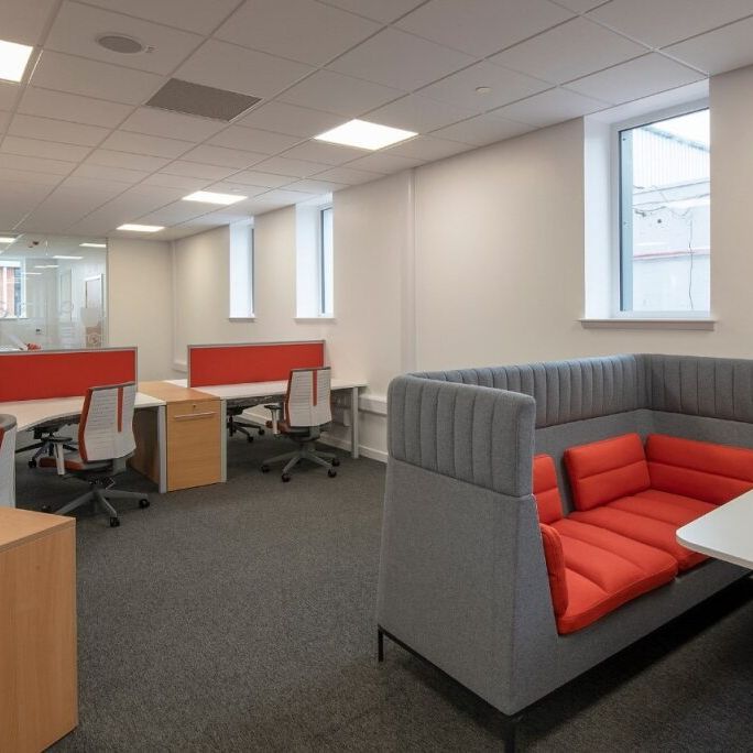 Modern open-plan office with desks, chairs, and a booth with red cushions