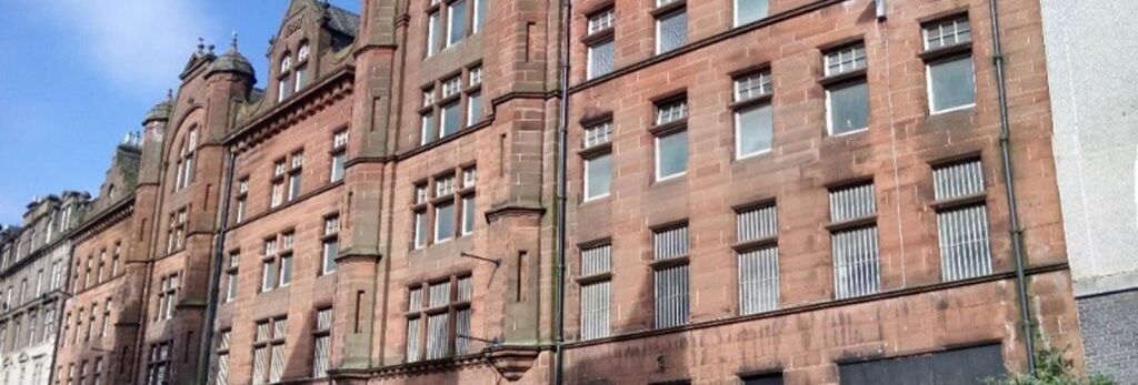 Large historic red sandstone building with multiple windows and decorative architectural features on a city street.