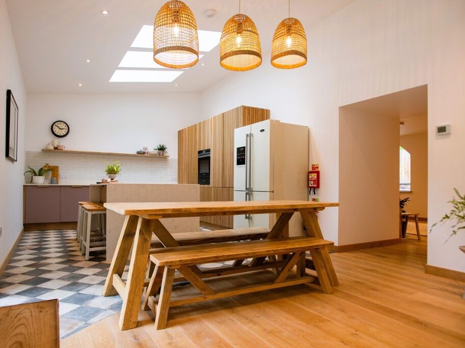Modern kitchen and dining area with wooden benches, large refrigerator, and pendant lights.
