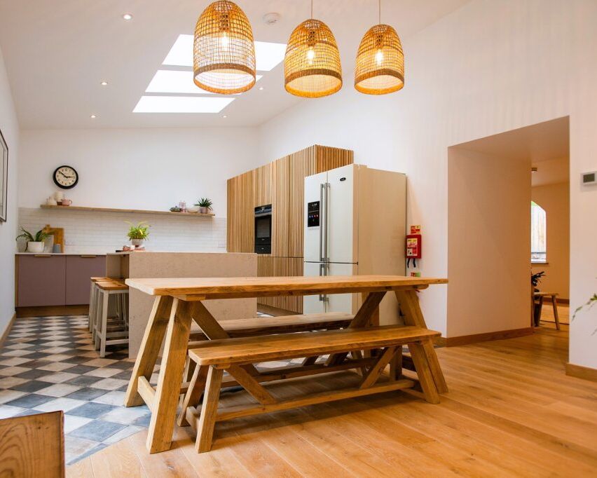 Modern kitchen and dining area with wooden benches, large refrigerator, and pendant lights.