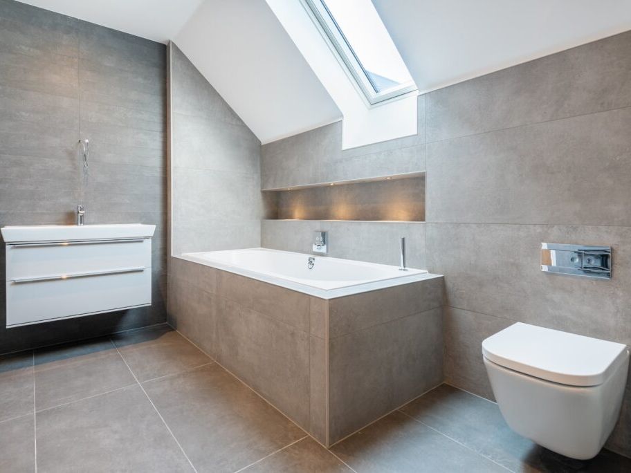Modern bathroom with gray tiles, a bathtub, floating vanity, and wall-mounted toilet