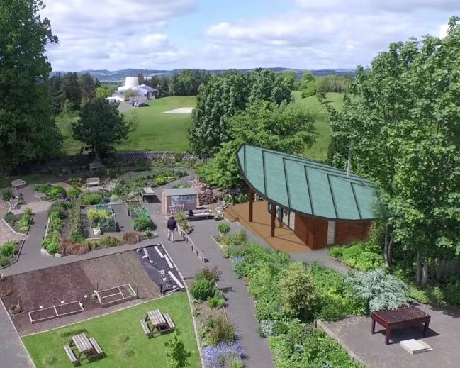 Aerial view of a public community garden with a modern green-roofed pavilion surrounded by trees and walking paths.