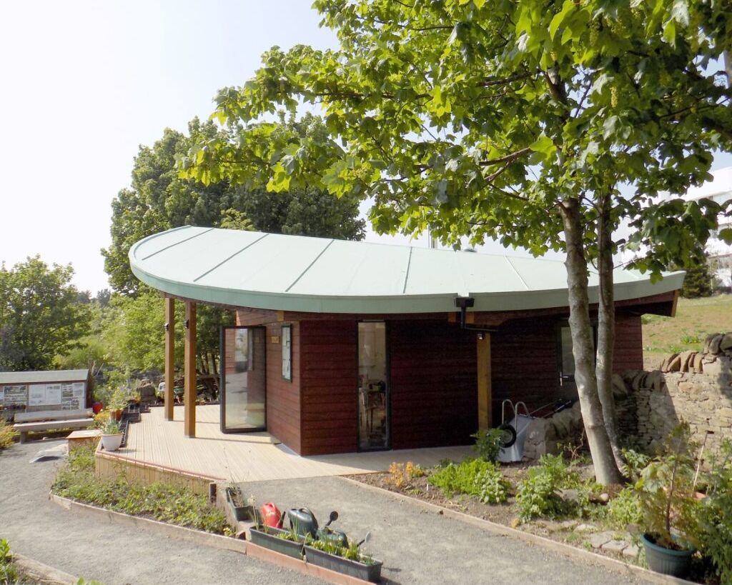 Small eco-friendly building with a curved roof surrounded by trees and a garden