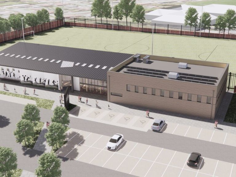 Aerial view of a modern sports facility with adjacent football fields and parking lot