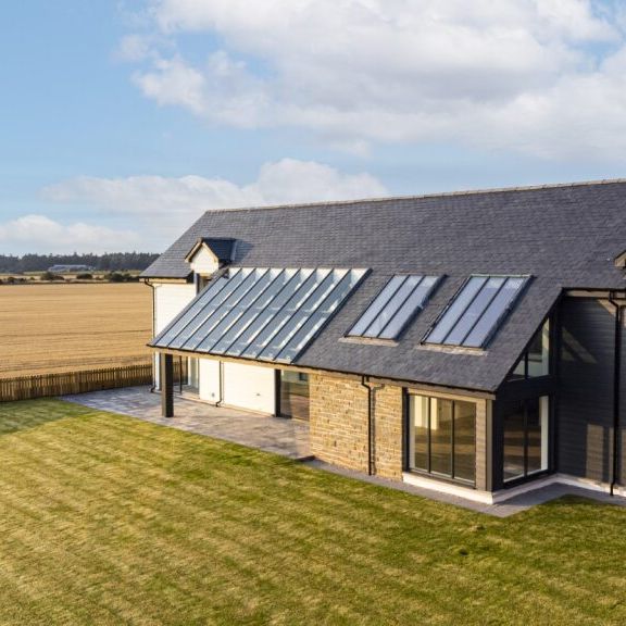 Modern farmhouse with large windows and dark exterior situated in a rural field