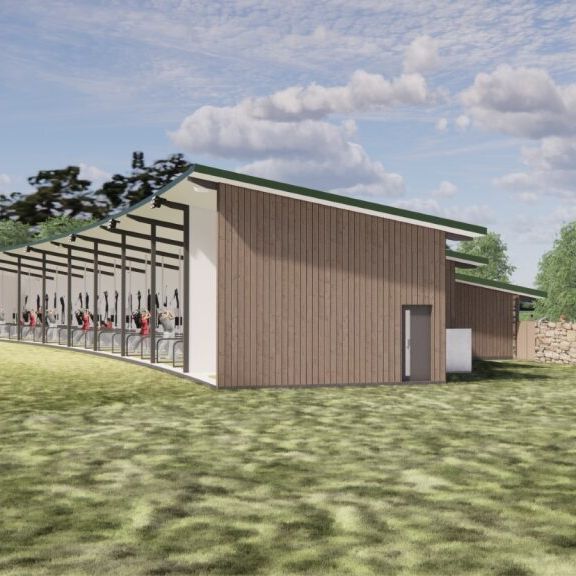 Modern open-air golf driving range building with wood panel siding, adjacent to a stone wall and green lawn under a partly cloudy sky.