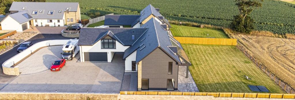 Aerial view of modern houses with well-maintained lawns and farmland in the background