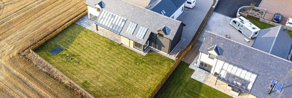 Aerial view of modern houses with large green lawns next to farmland