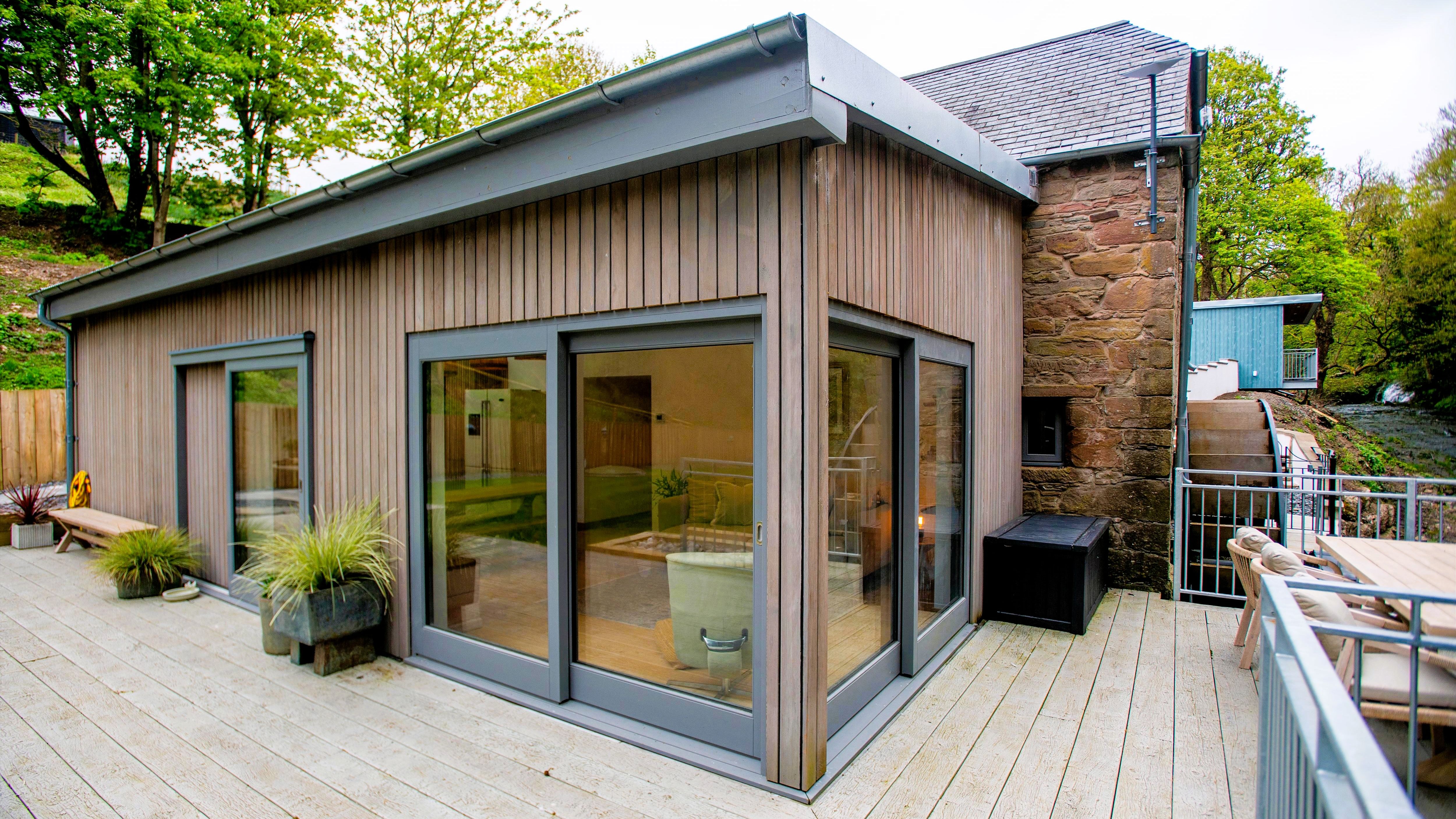 Modern wooden exterior of a renovated building with large glass windows and outdoor patio seating.