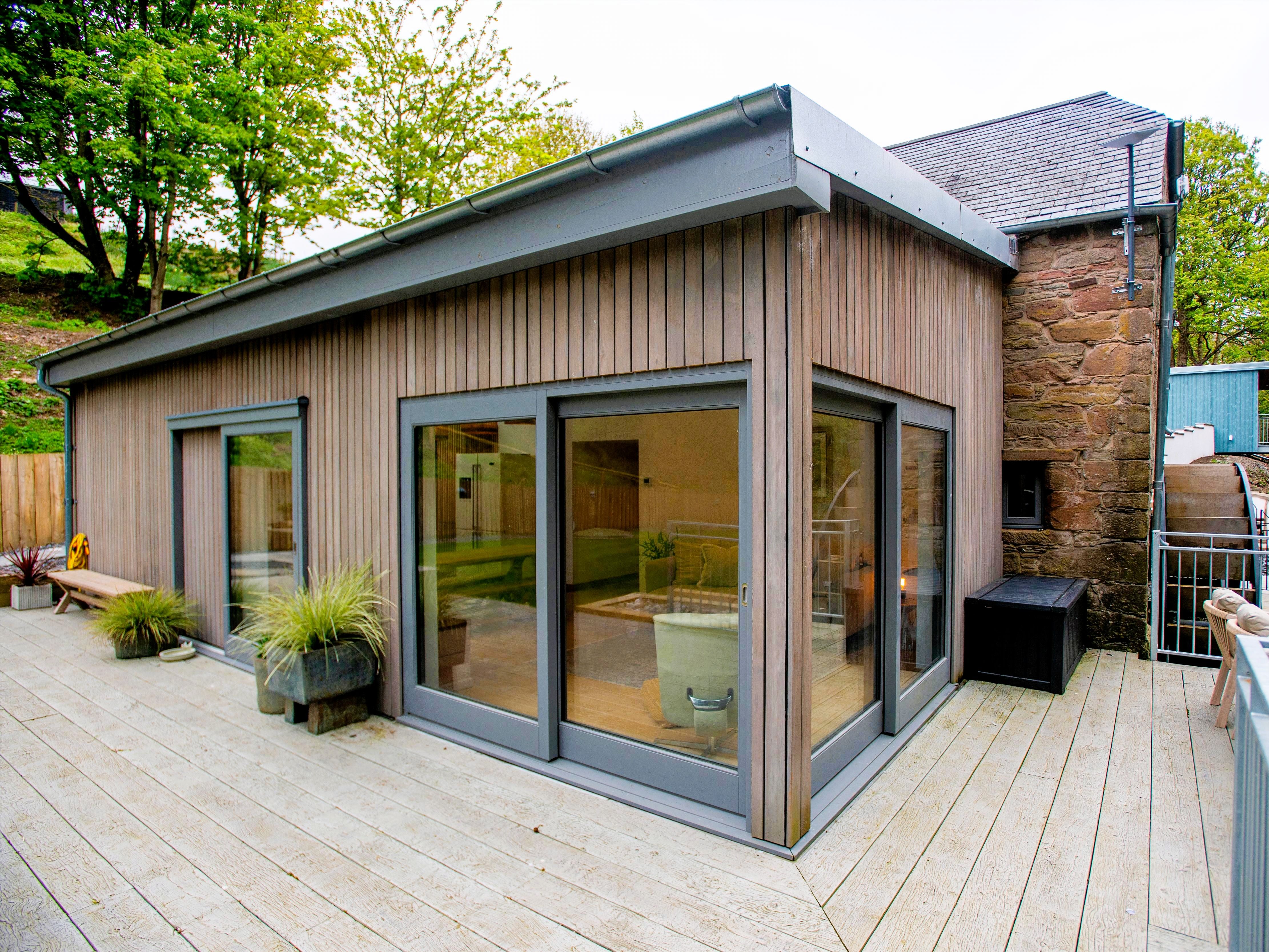 Modern wooden exterior of a renovated building with large glass windows and outdoor patio seating.