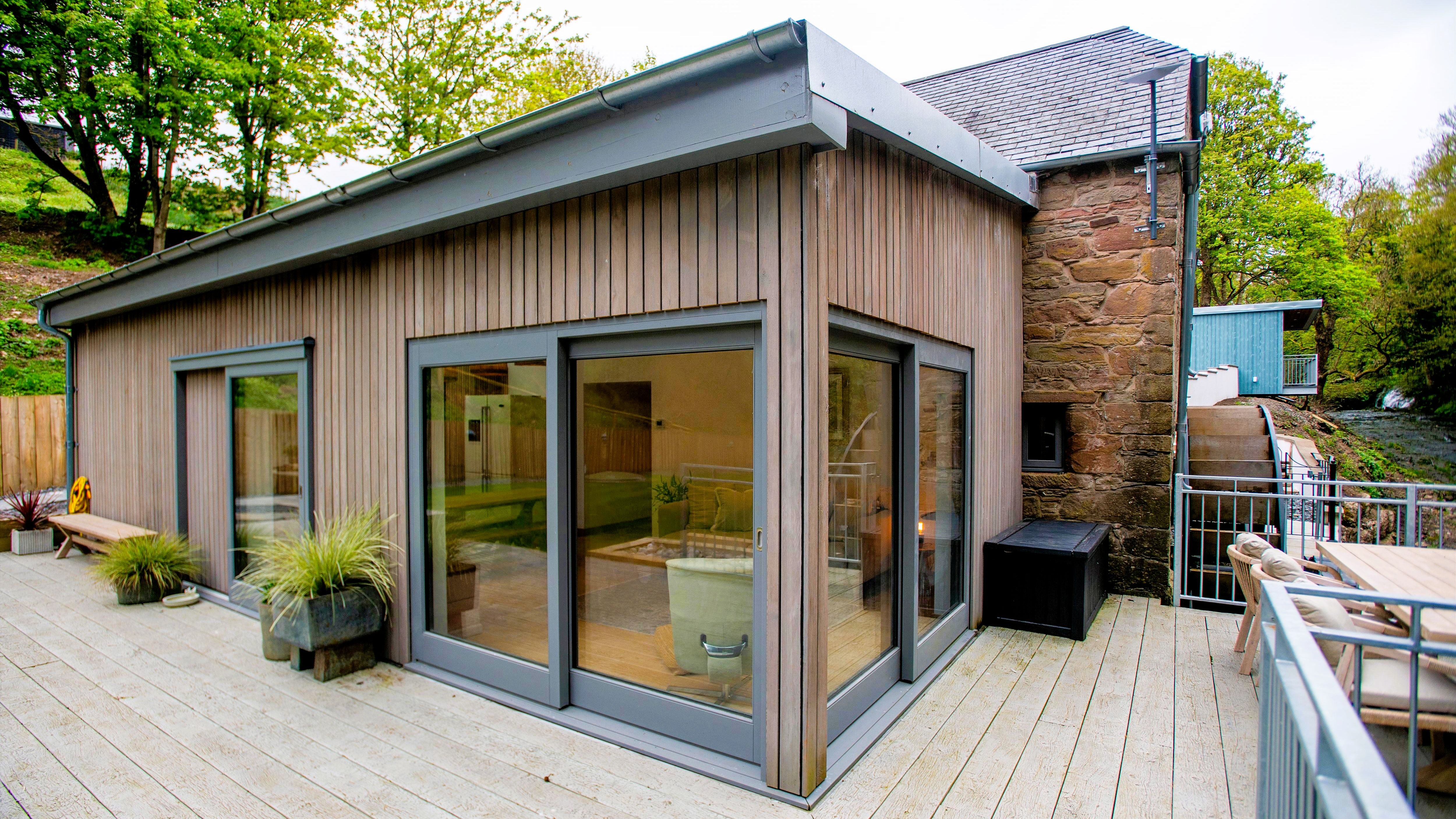 Modern wooden exterior of a renovated building with large glass windows and outdoor patio seating.