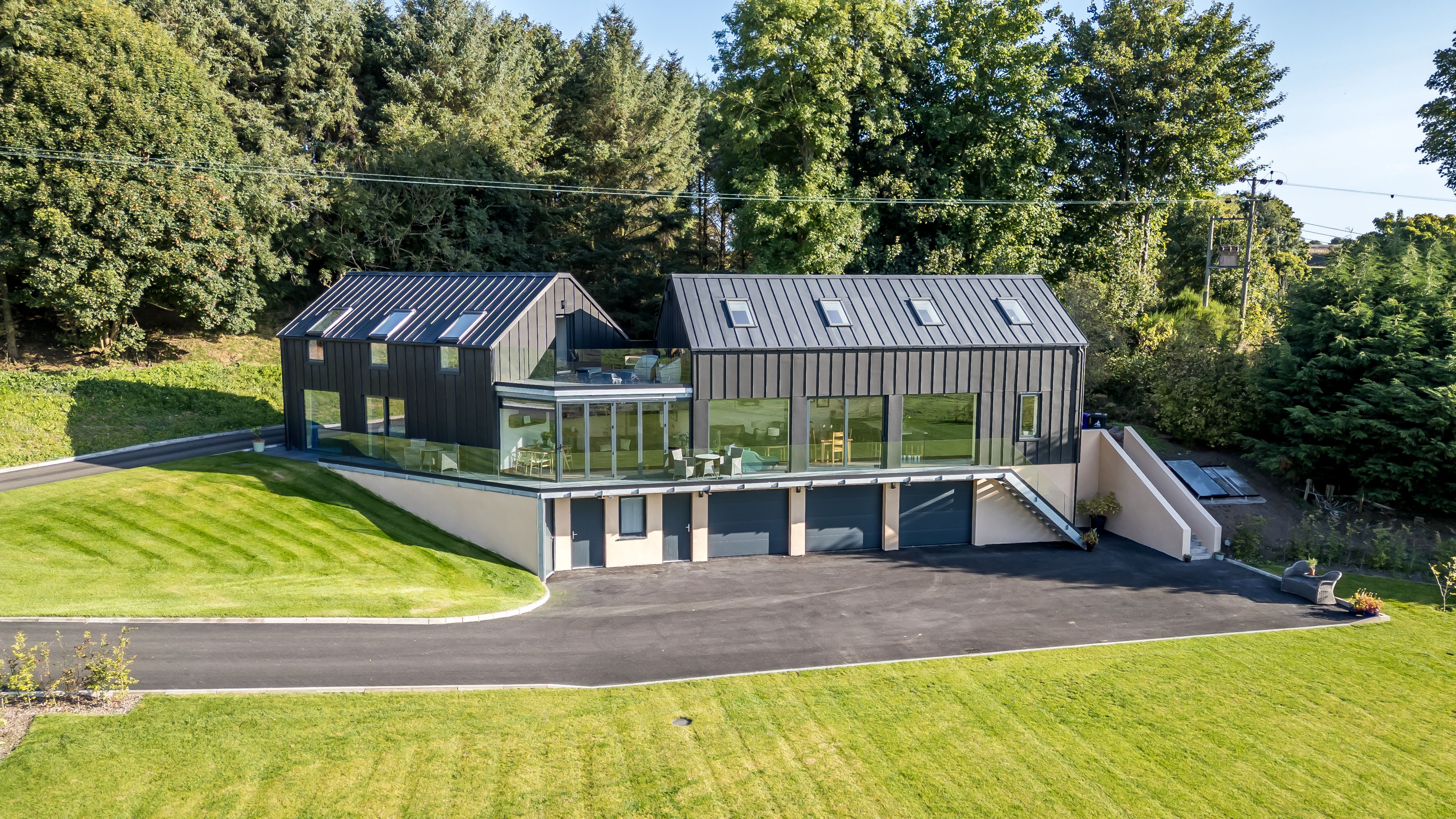 Modern house with black metal roof and large glass windows surrounded by green lawn and trees