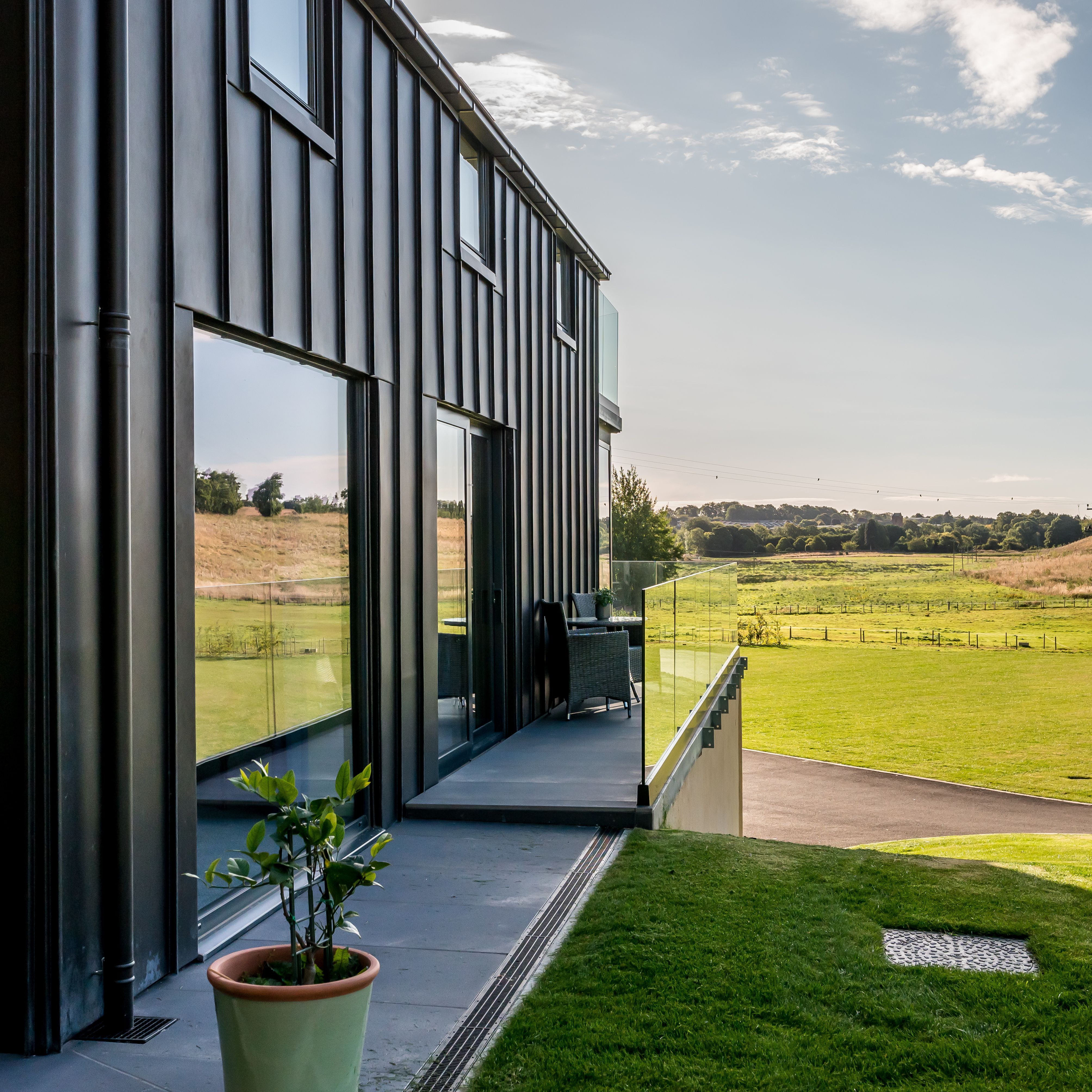 Modern building exterior with glass balcony overlooking green fields and hills on a sunny day