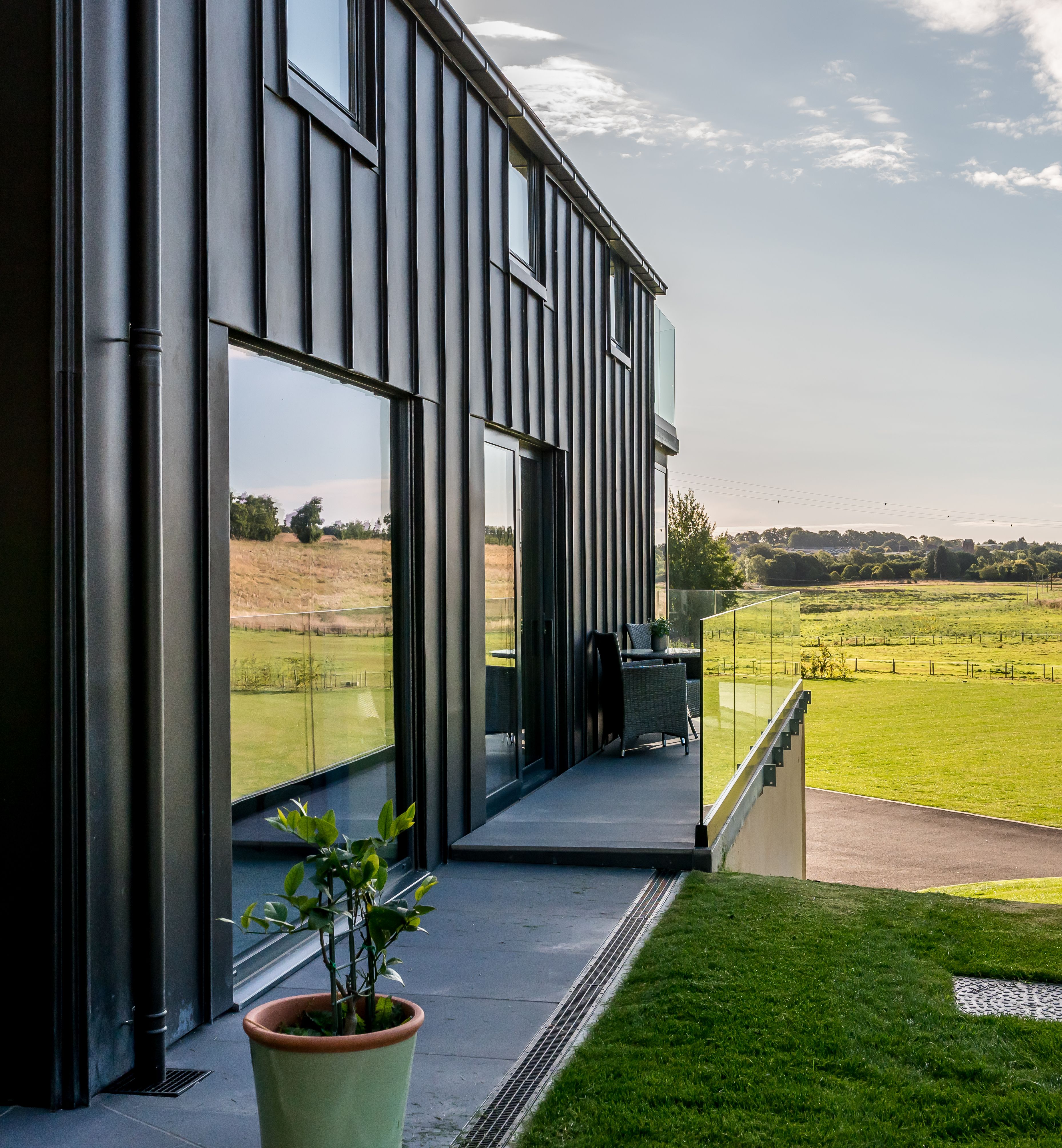 Modern building exterior with glass balcony overlooking green fields and hills on a sunny day