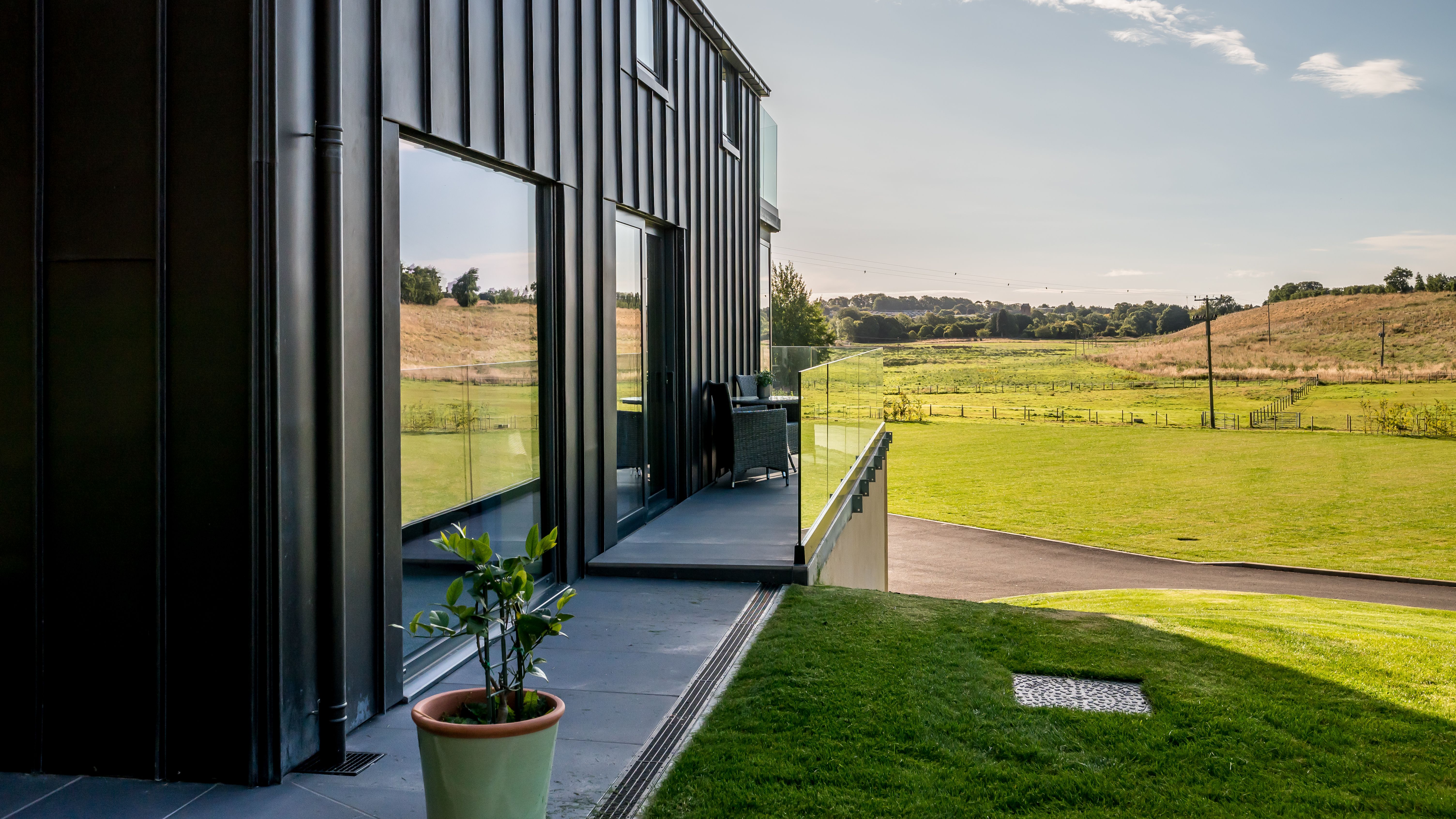 Modern building exterior with glass balcony overlooking green fields and hills on a sunny day