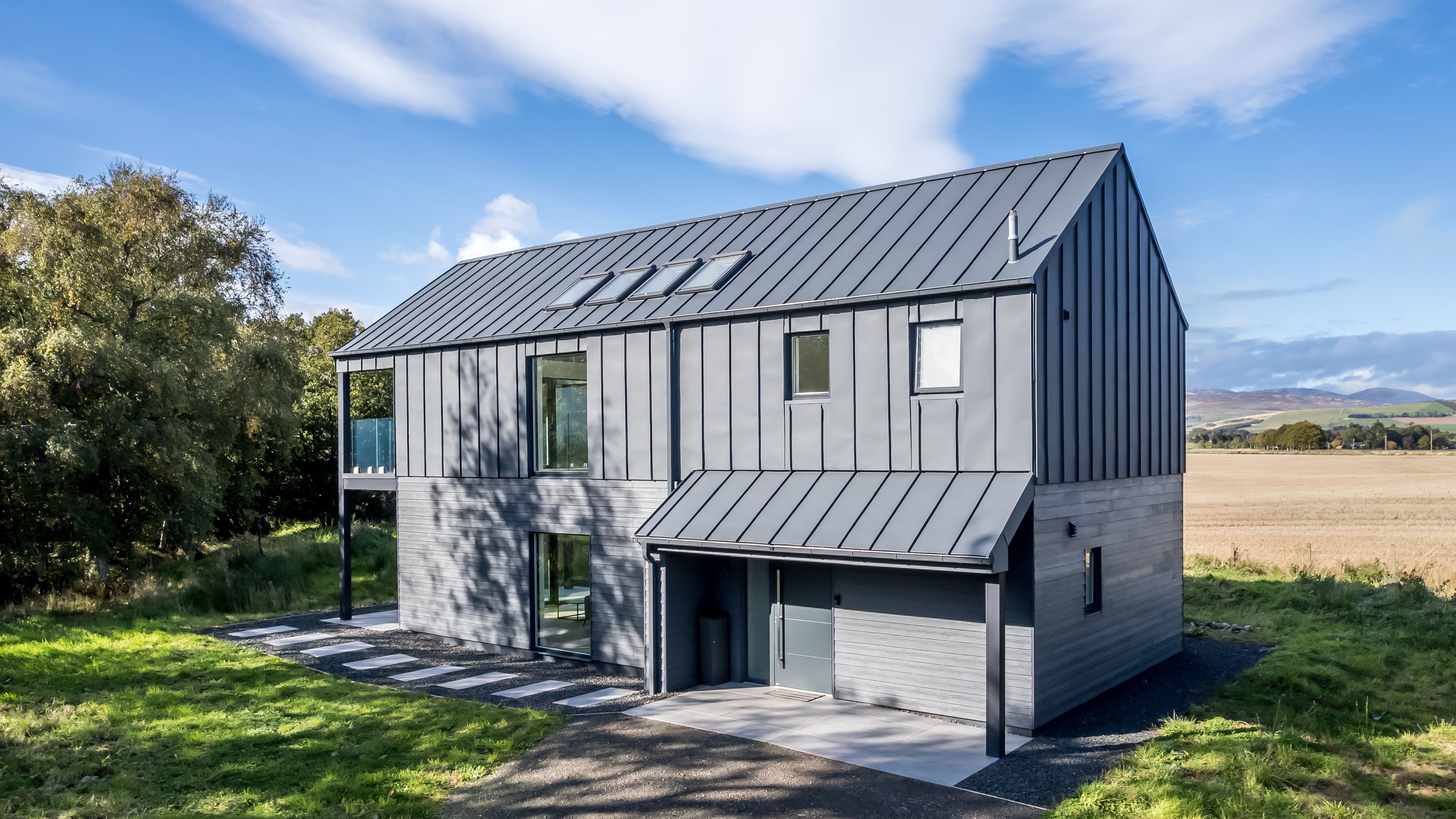 Modern black barn-style house with metal roof surrounded by trees and open fields