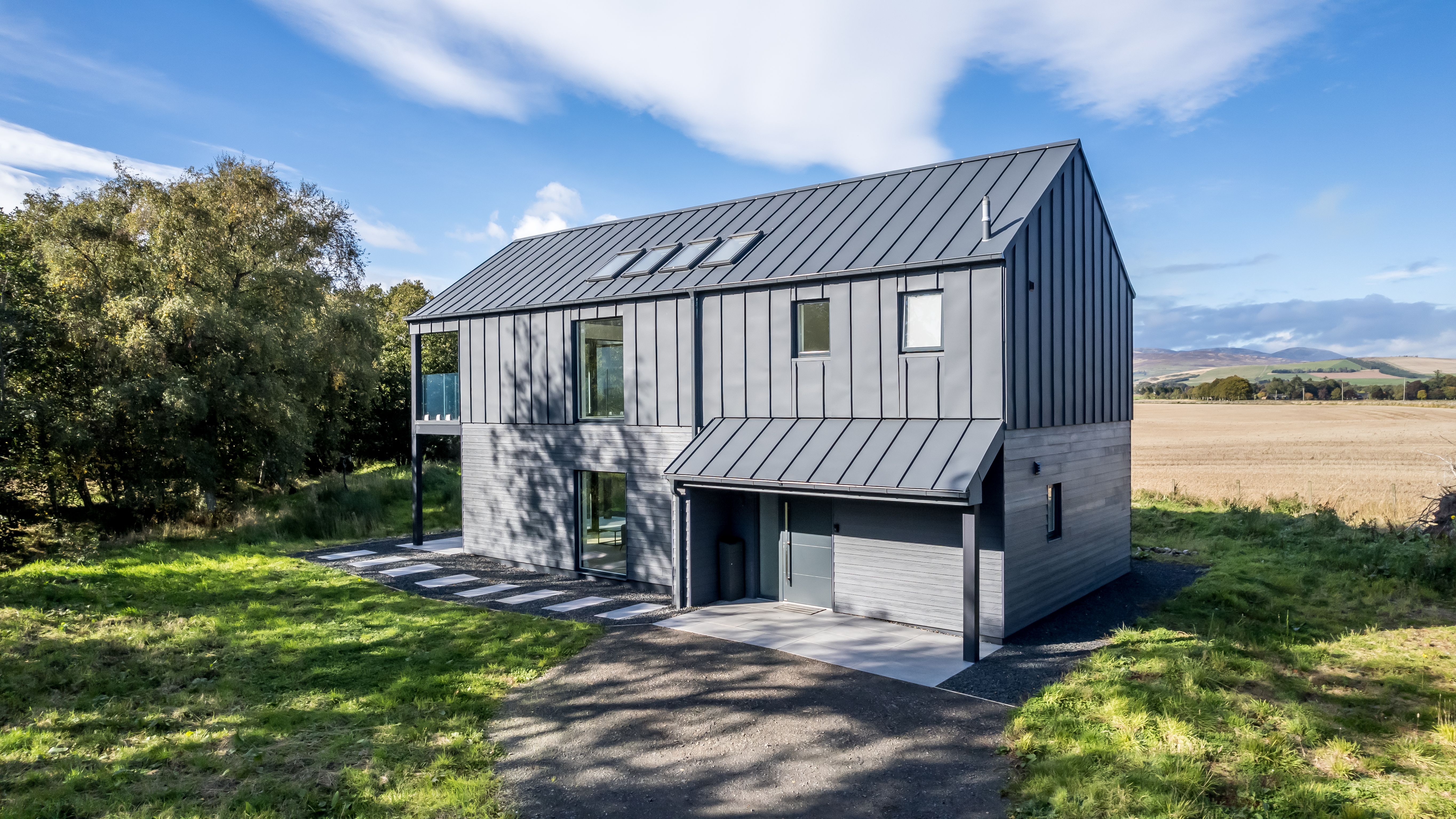 Modern black barn-style house with metal roof surrounded by trees and open fields