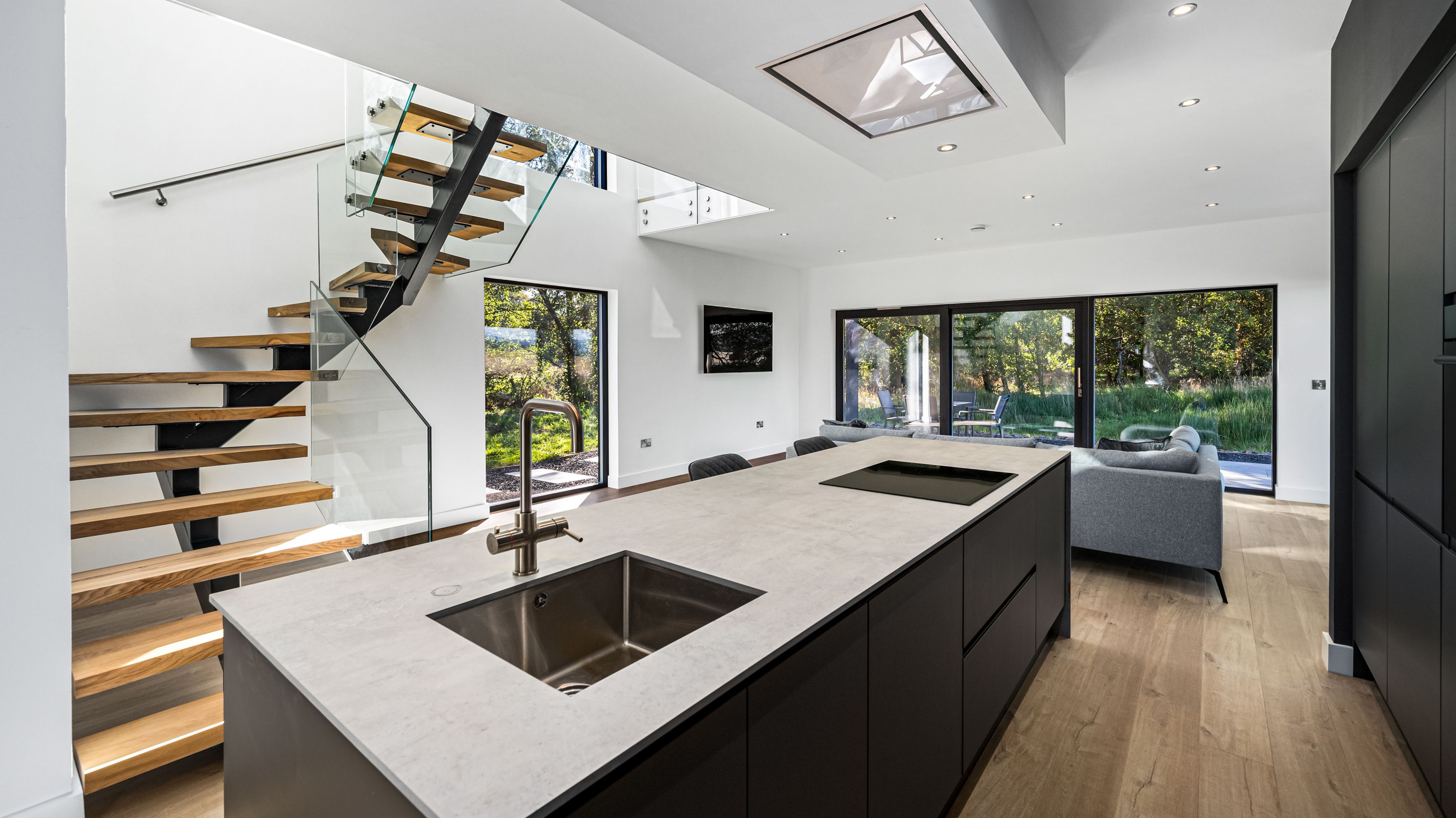 Modern open-plan kitchen and living area with large windows and a floating staircase