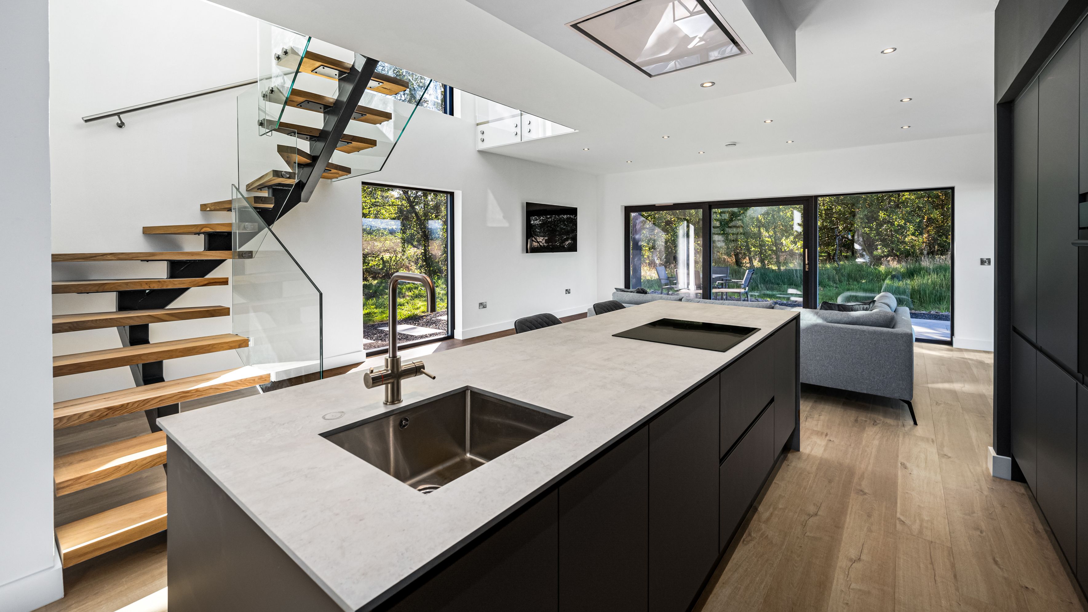 Modern open-plan kitchen and living area with large windows and a floating staircase