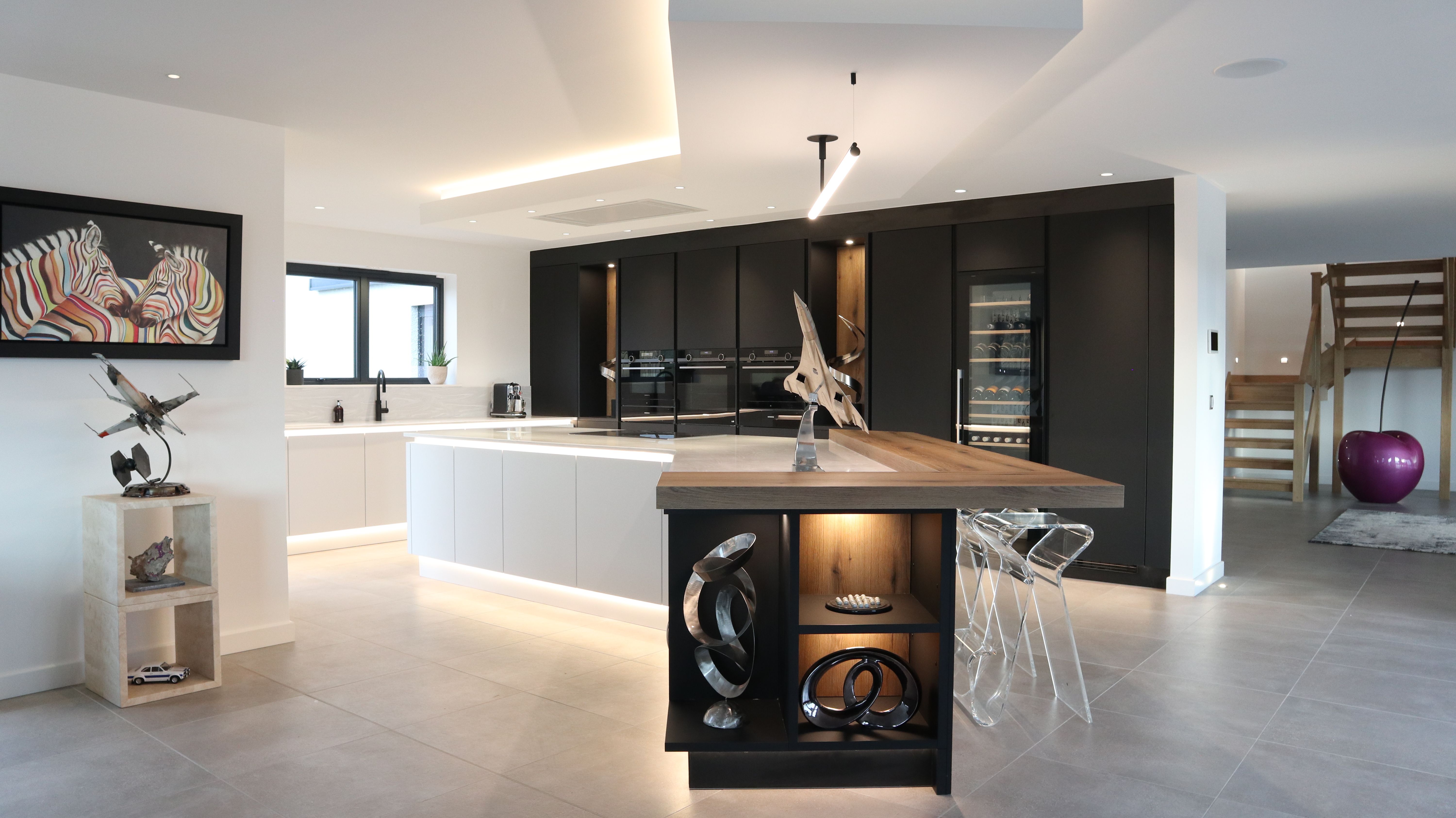 Modern kitchen with black cabinets, white island, wooden accents, and decorative art pieces