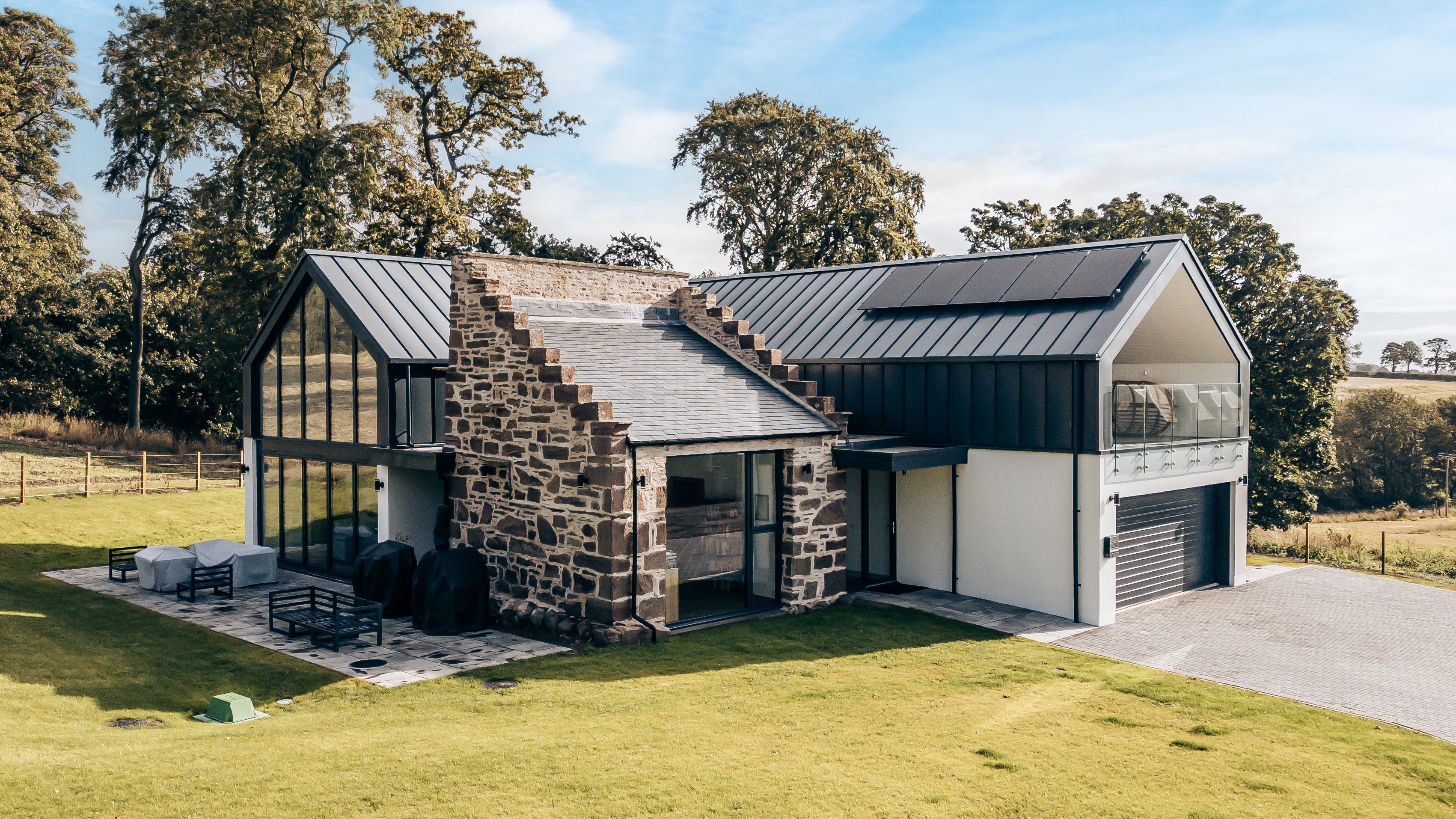 Modern house with large glass windows and a mix of stone and metal exterior surrounded by green lawn and trees