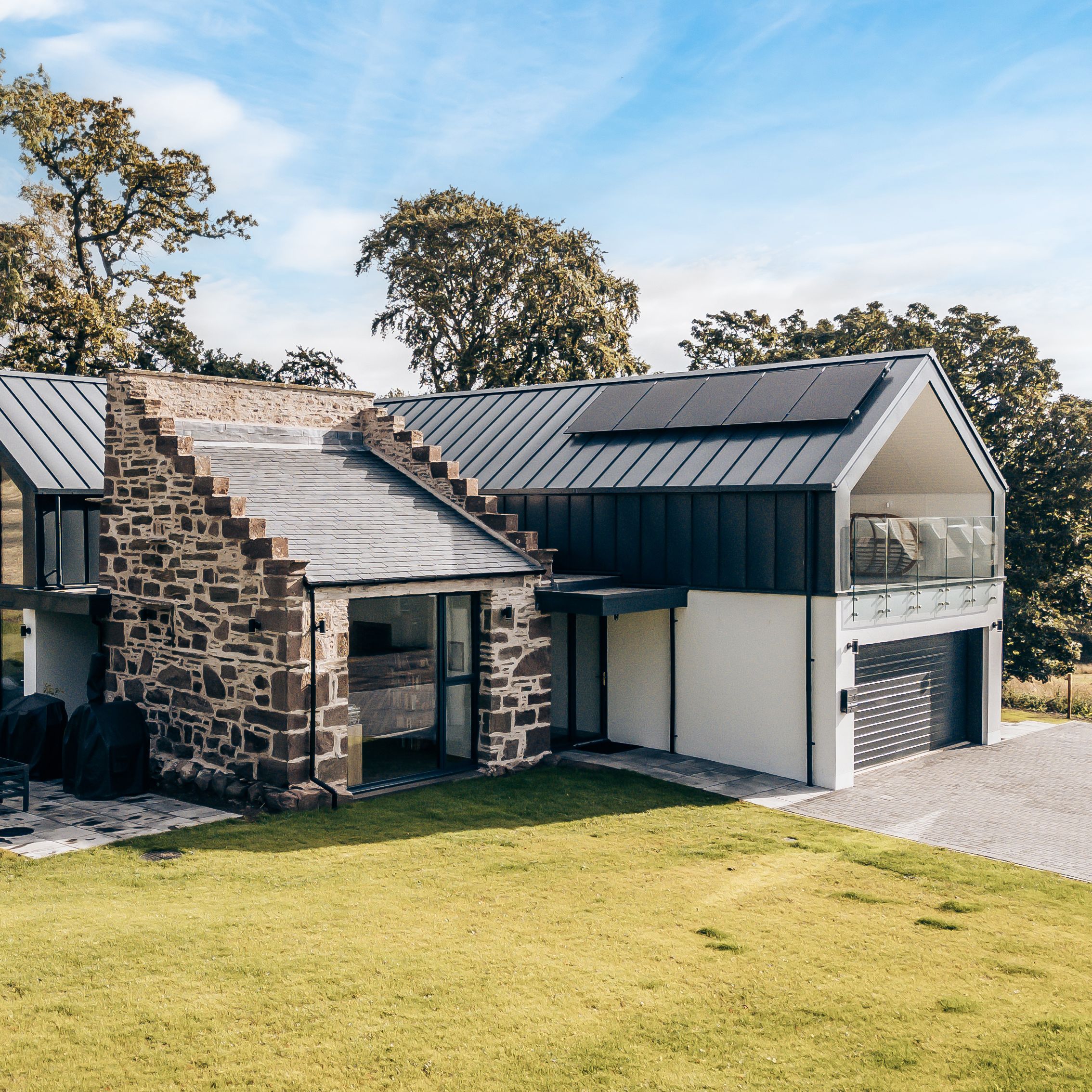 Modern house with large glass windows and a mix of stone and metal exterior surrounded by green lawn and trees
