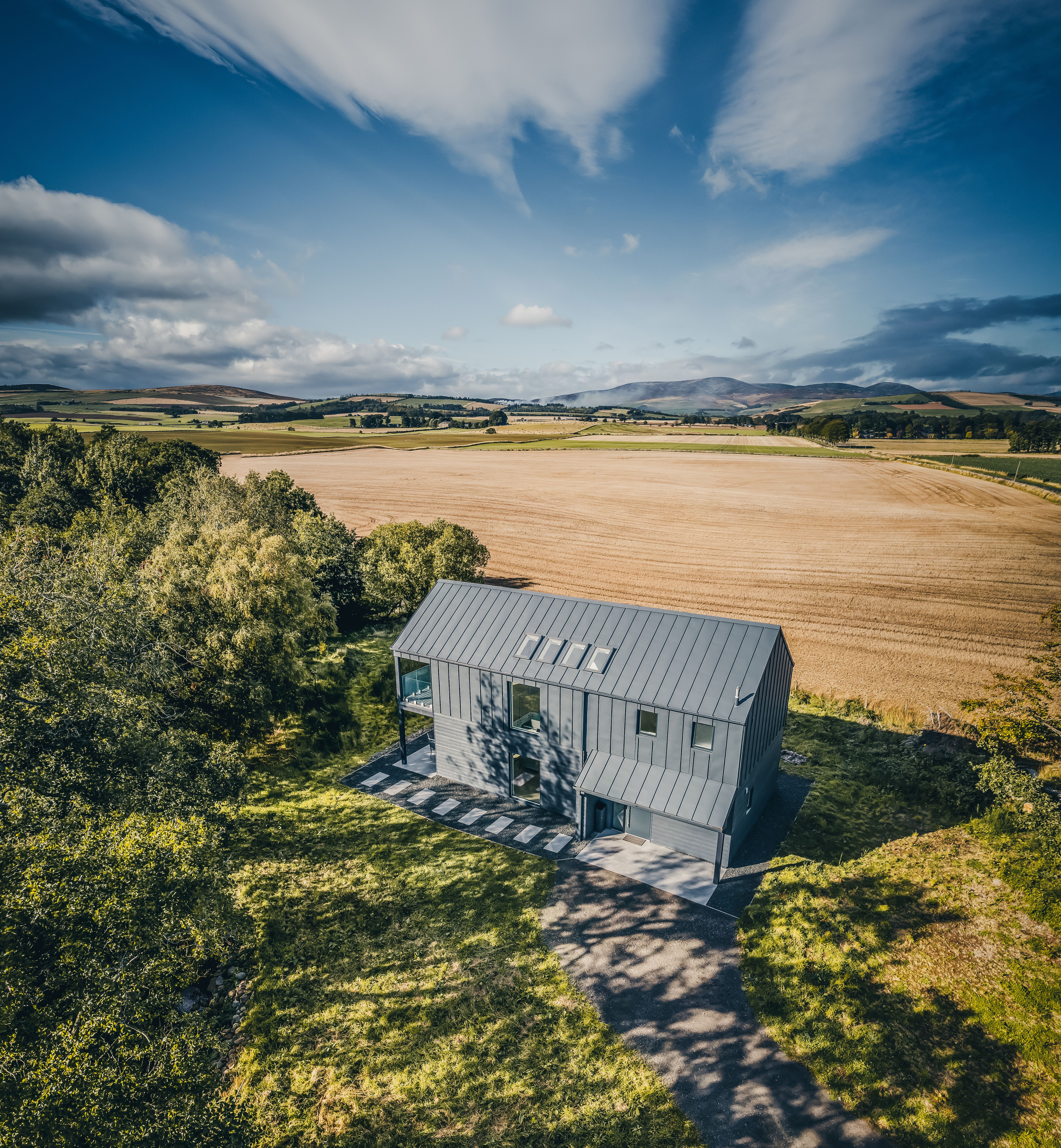 Modern black barn-style house in a rural field with dramatic skies overhead