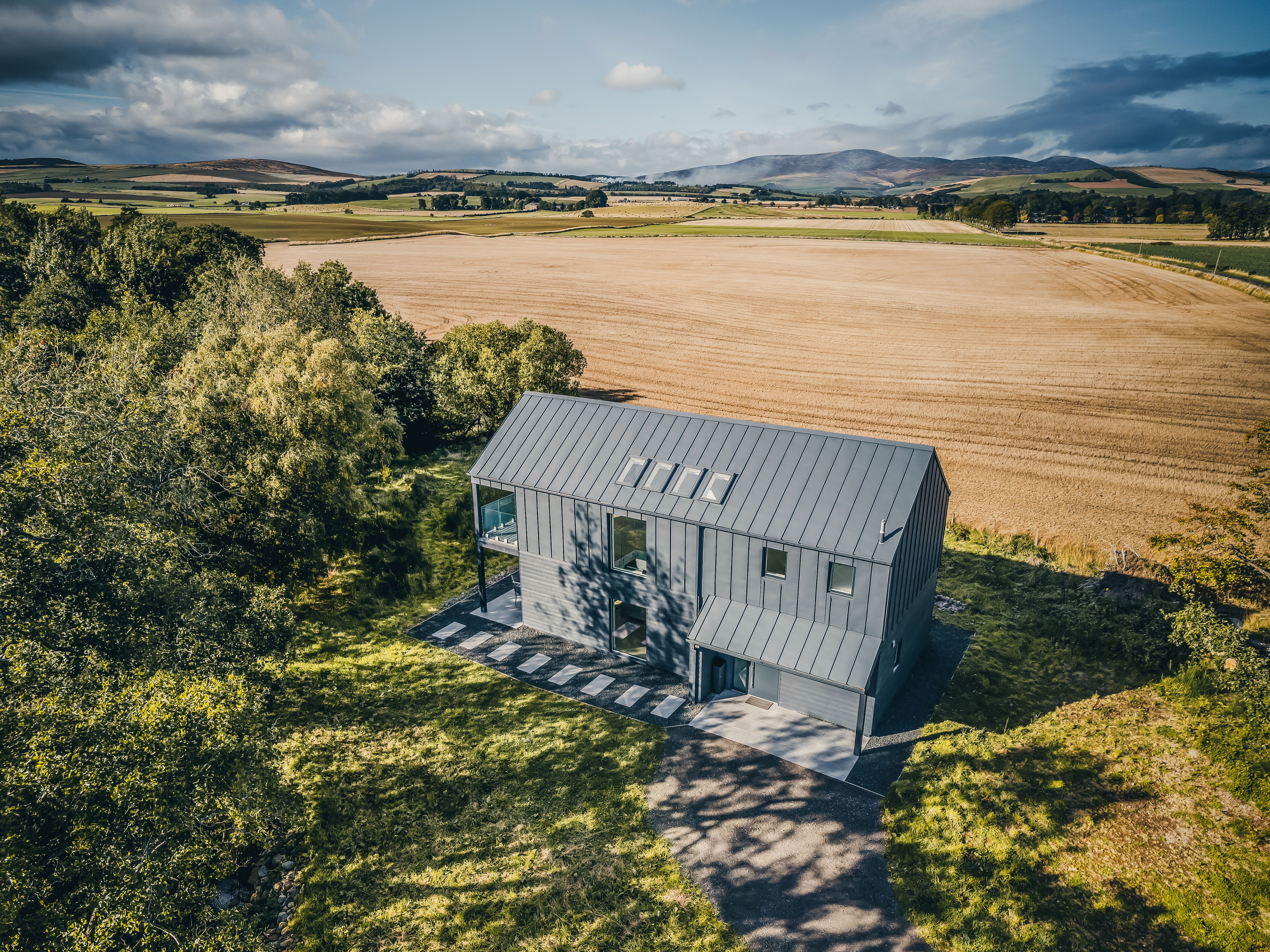 Modern black barn-style house in a rural field with dramatic skies overhead