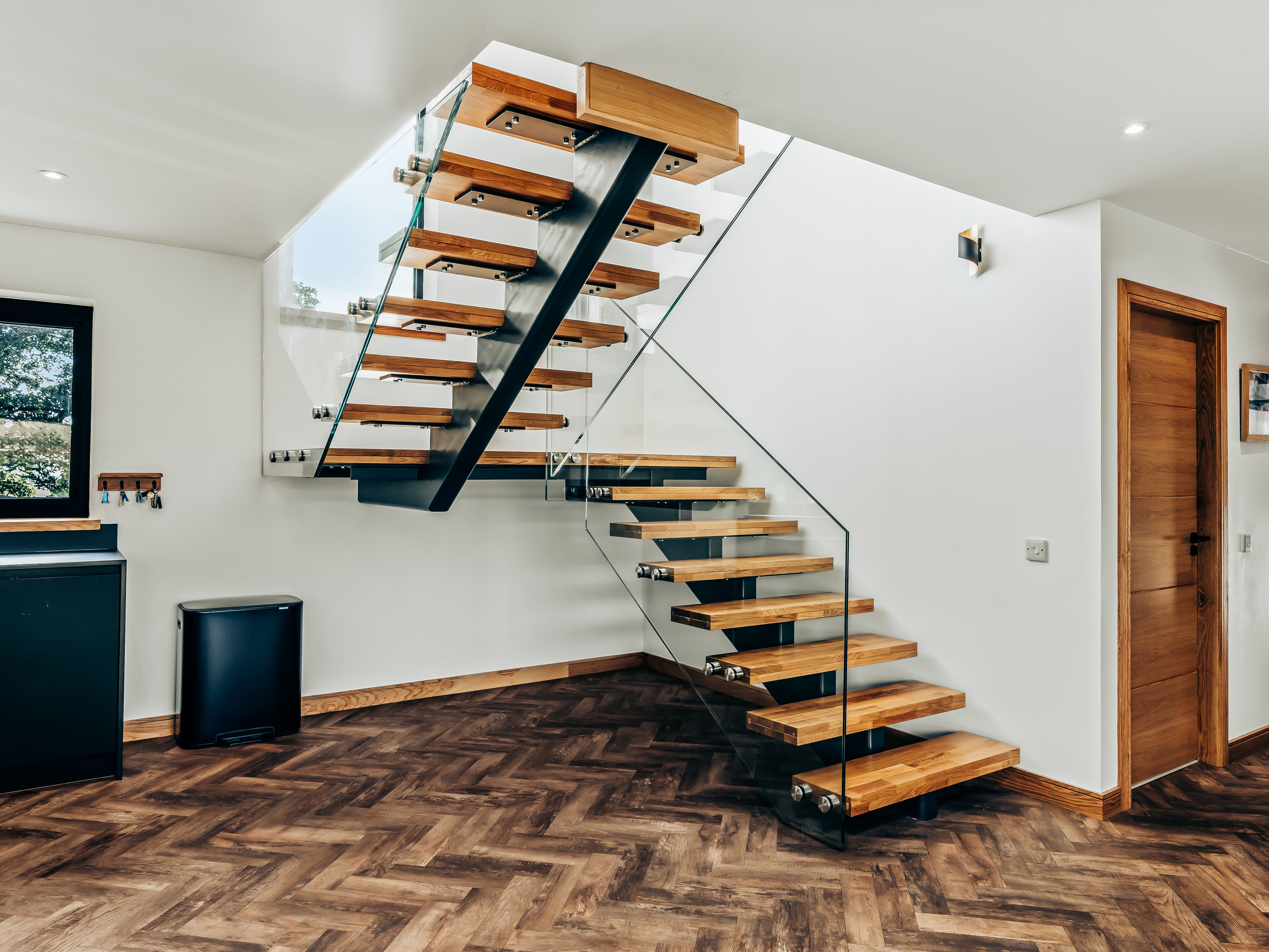 Modern staircase with wooden steps, glass railing, and chevron patterned wooden floor in a contemporary home interior