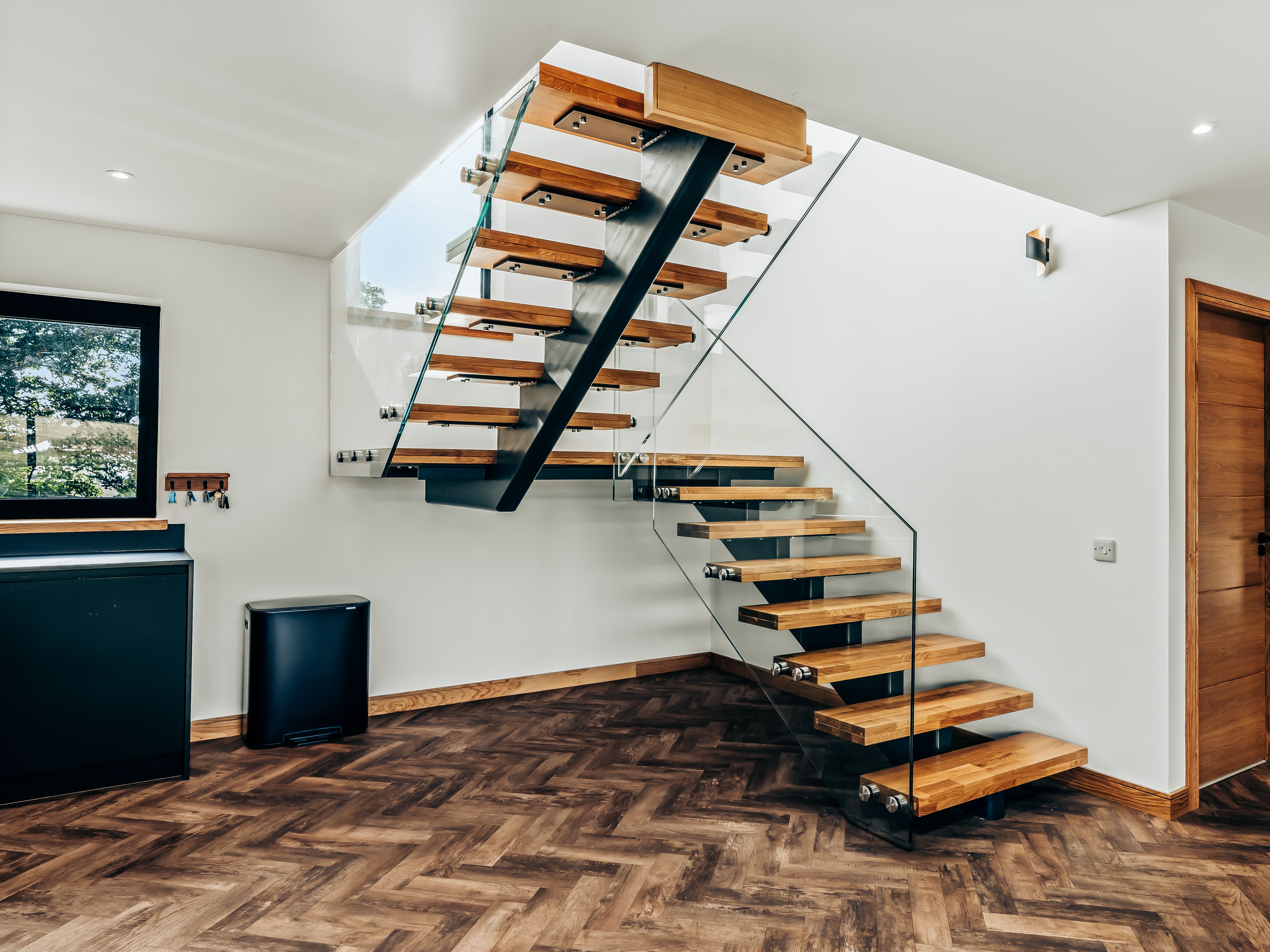 Modern staircase with wooden steps, glass railing, and chevron patterned wooden floor in a contemporary home interior
