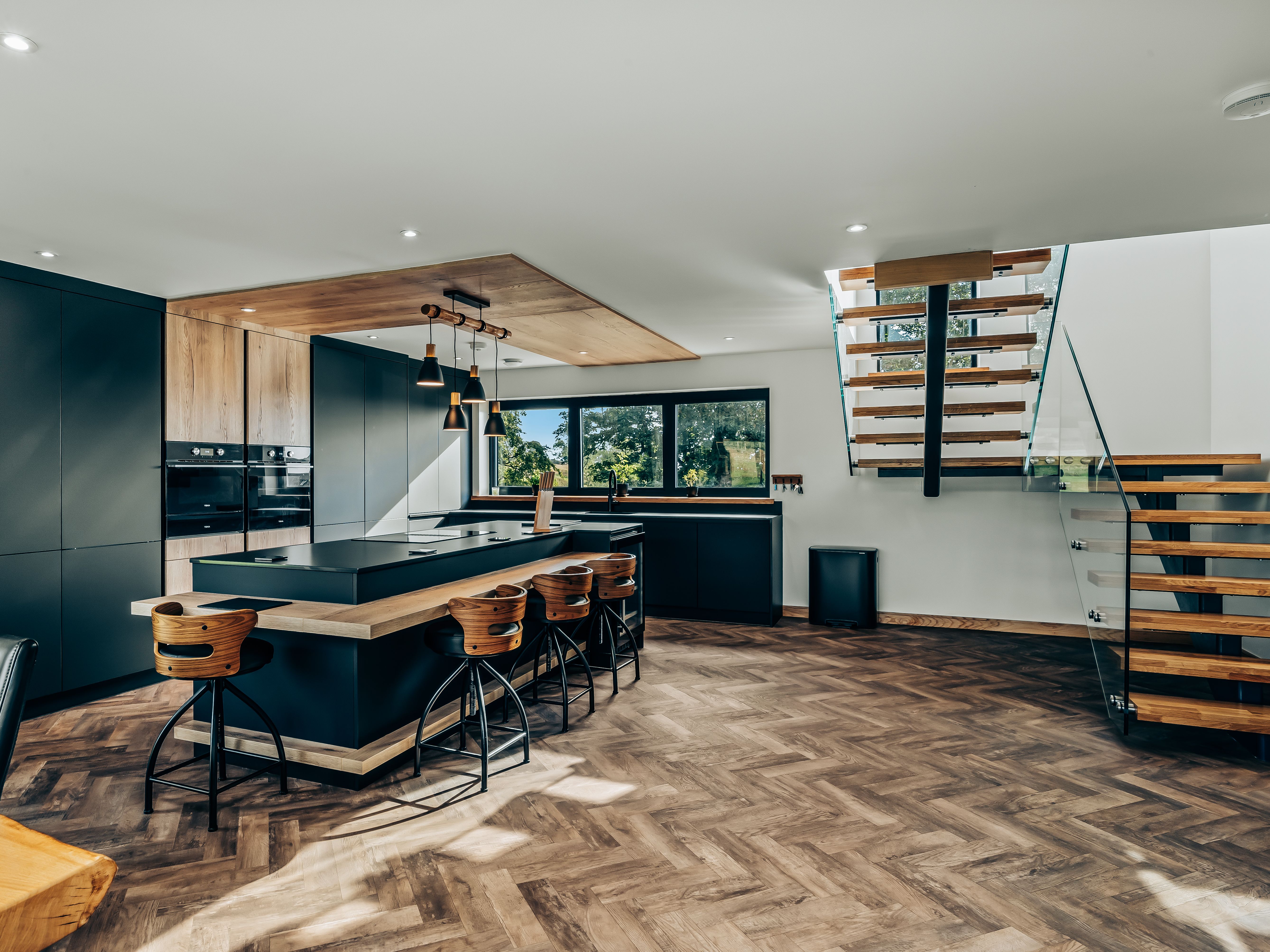 Modern kitchen interior with wooden flooring, large island, and floating staircase.
