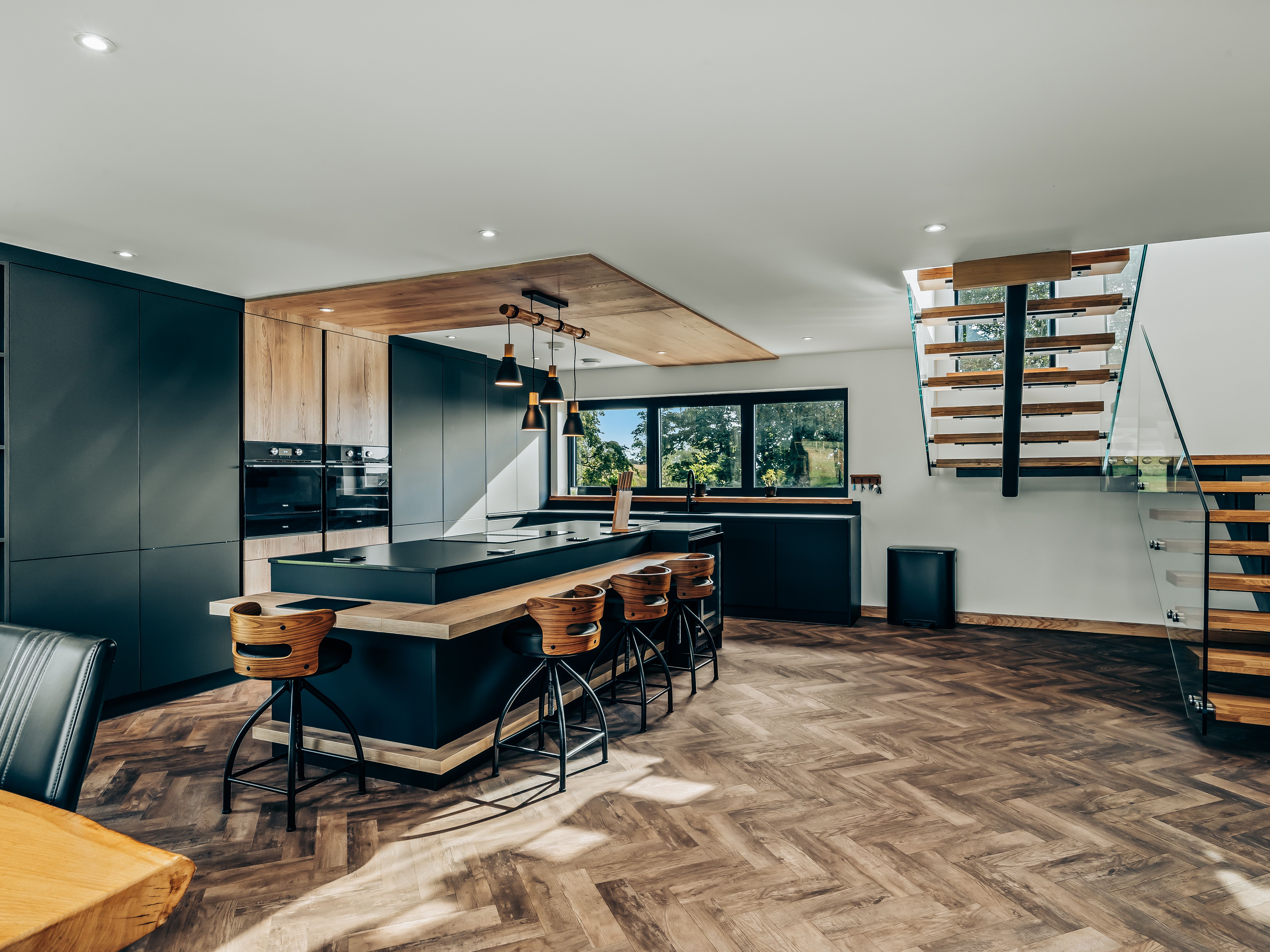 Modern kitchen interior with wooden flooring, large island, and floating staircase.