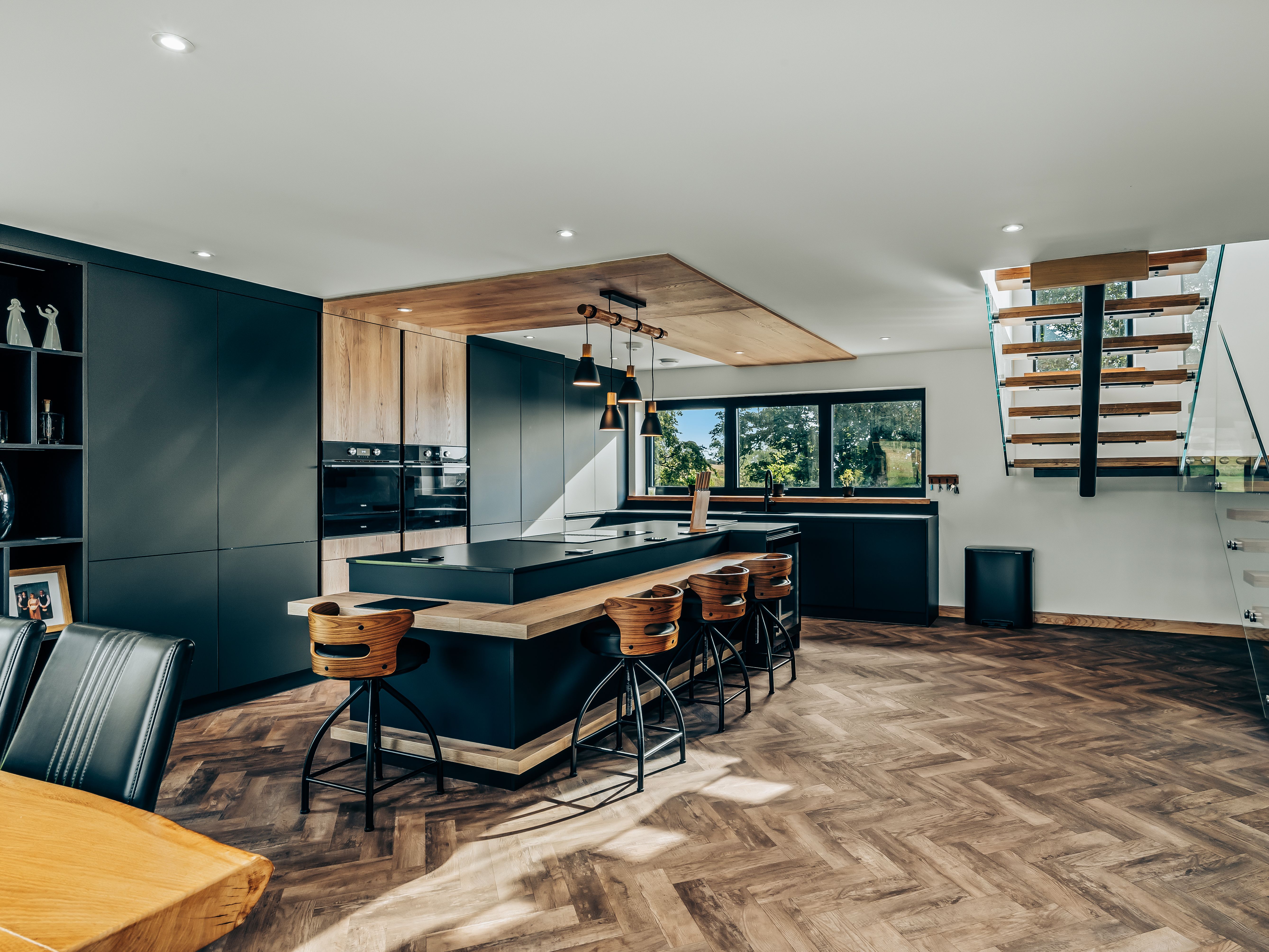 Modern kitchen interior with wooden flooring, large island, and floating staircase.