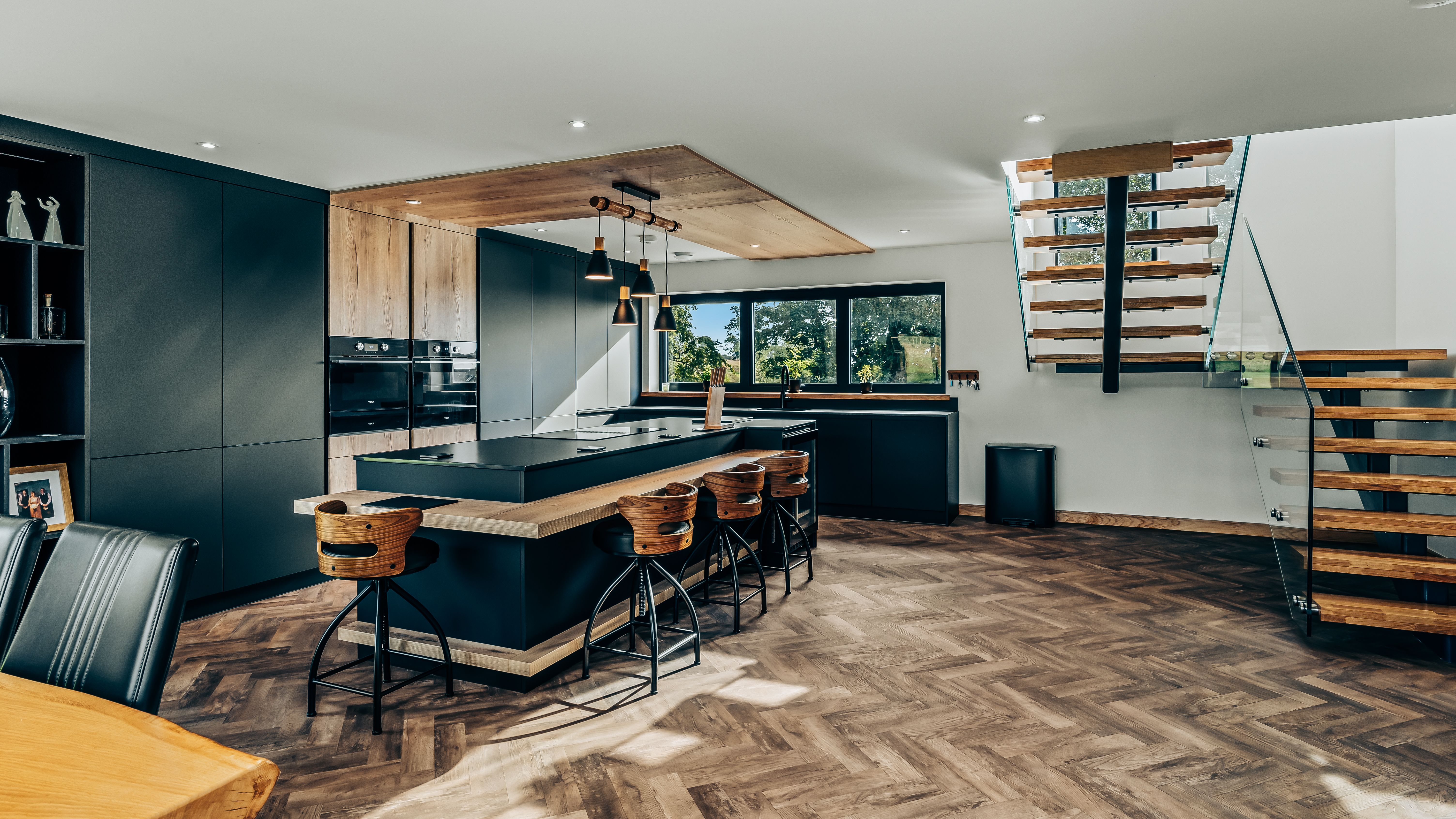 Modern kitchen interior with wooden flooring, large island, and floating staircase.