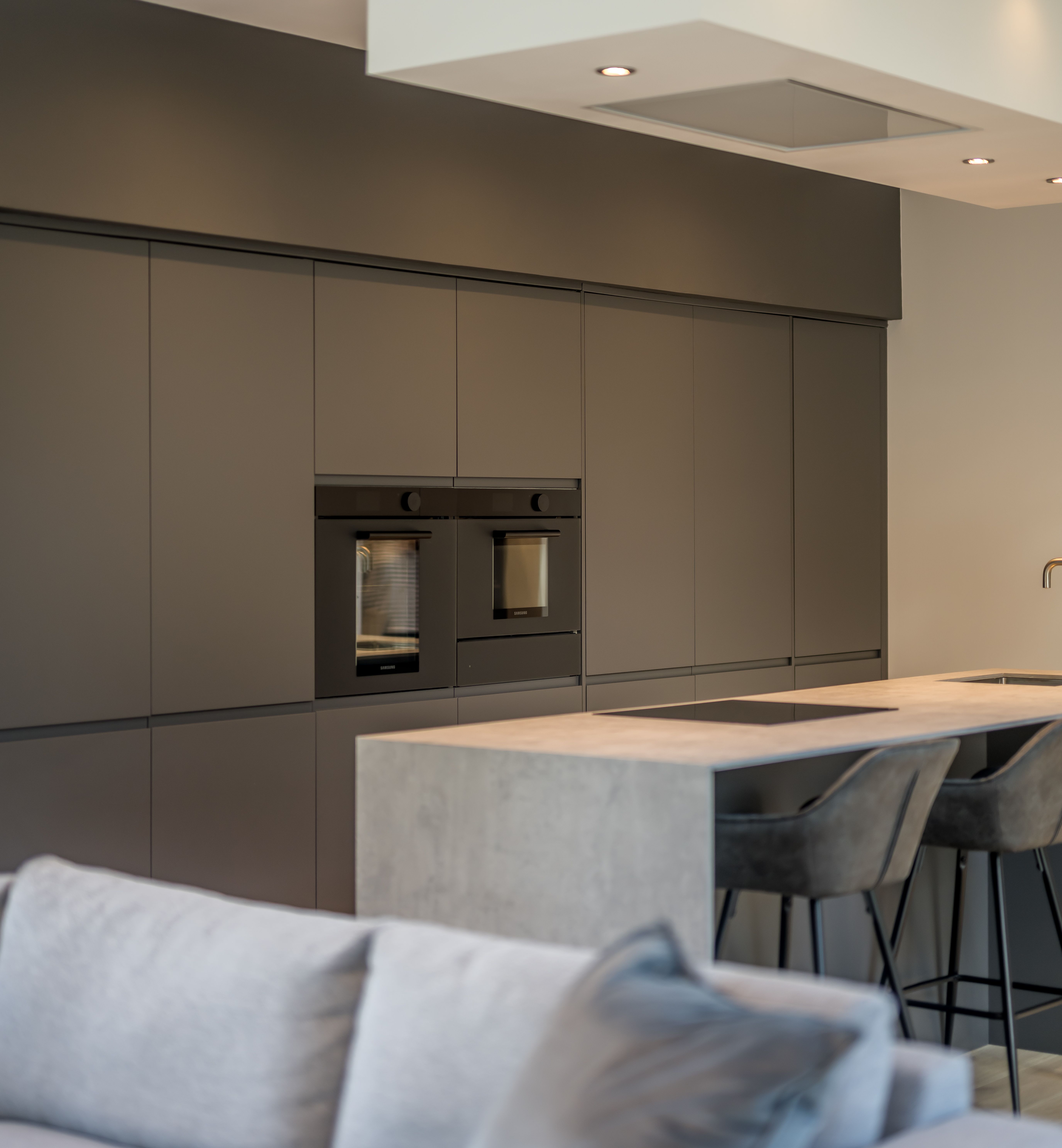 Modern kitchen with gray cabinetry, built-in ovens, and a concrete island with bar stools