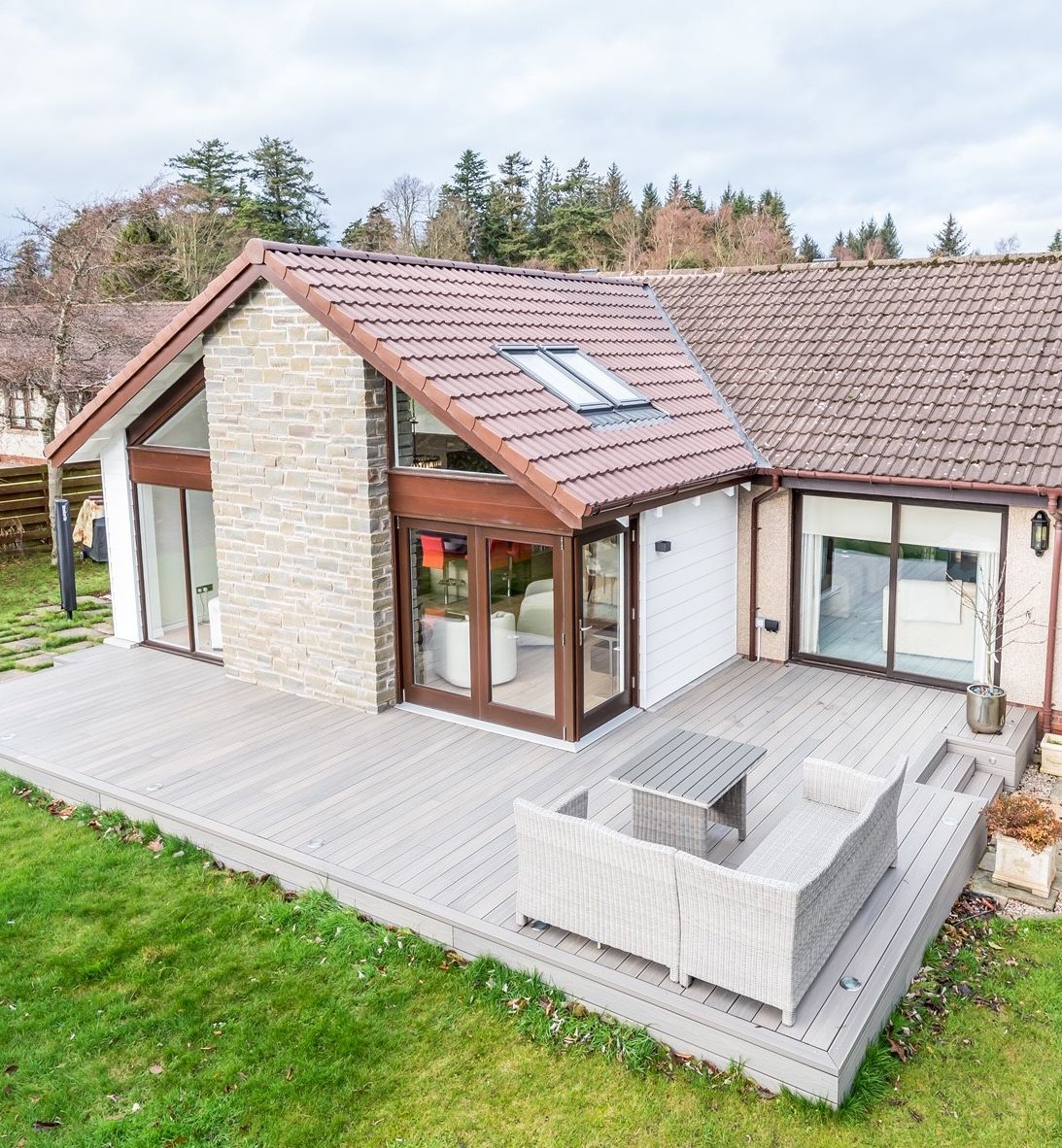 Modern house with stone and tile exterior, wooden deck, and outdoor seating area.