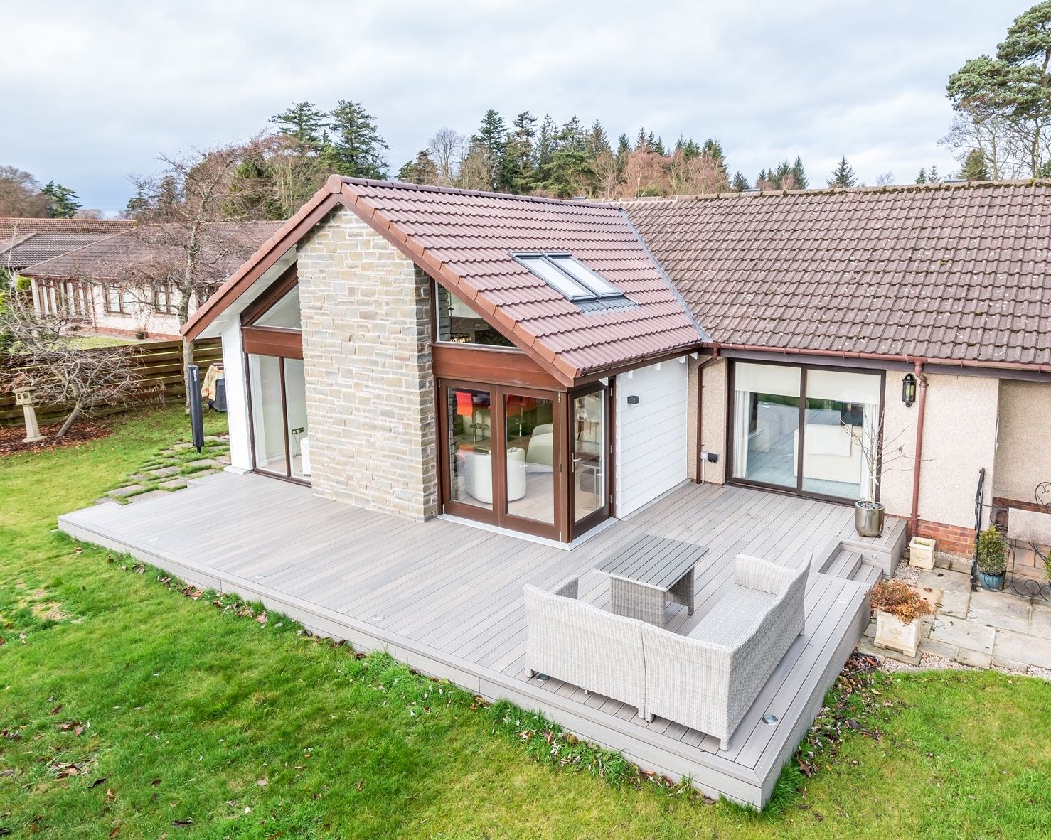 Modern house with stone and tile exterior, wooden deck, and outdoor seating area.
