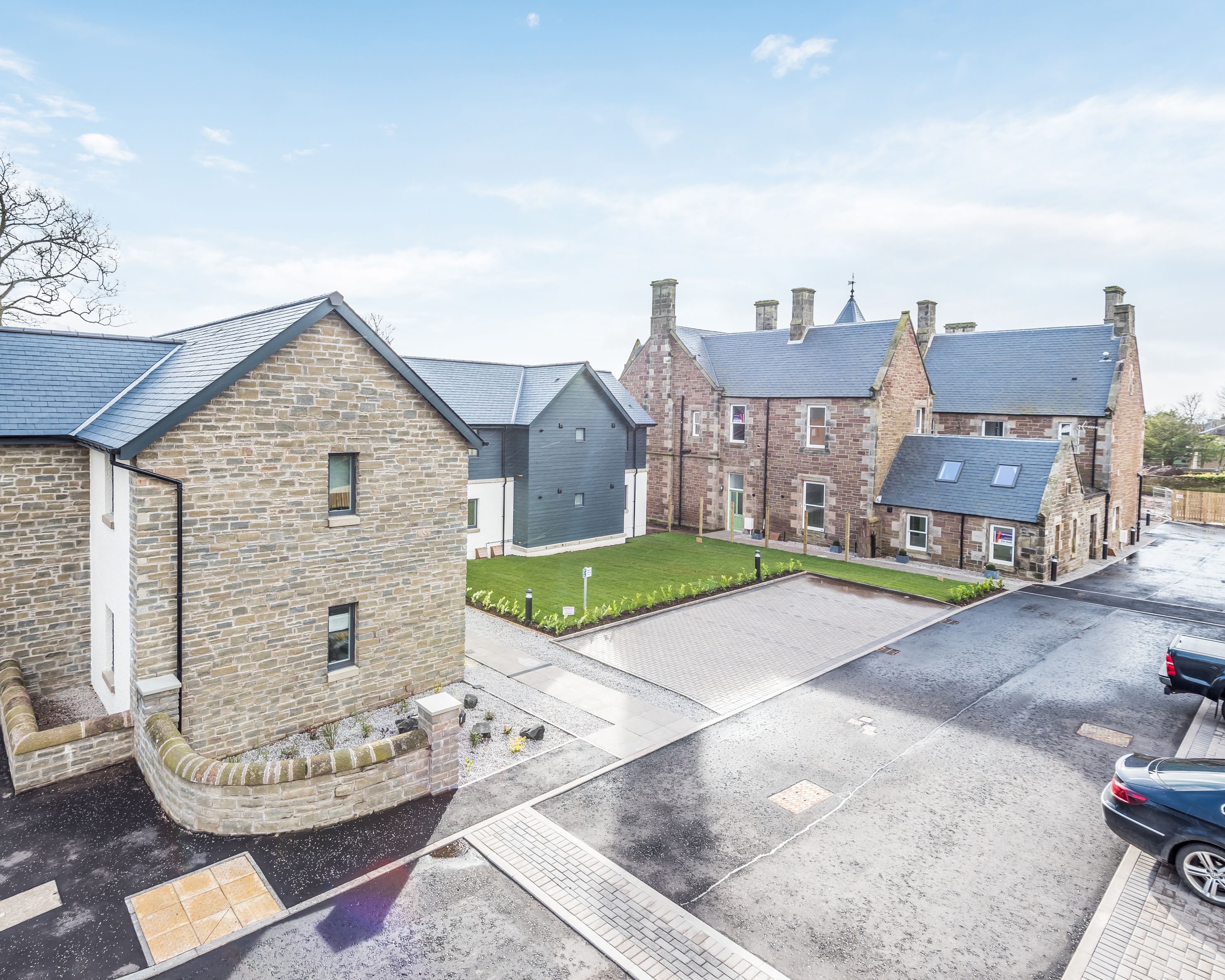 Modern stone buildings with slate roofs and a parking lot in front, on a clear day.