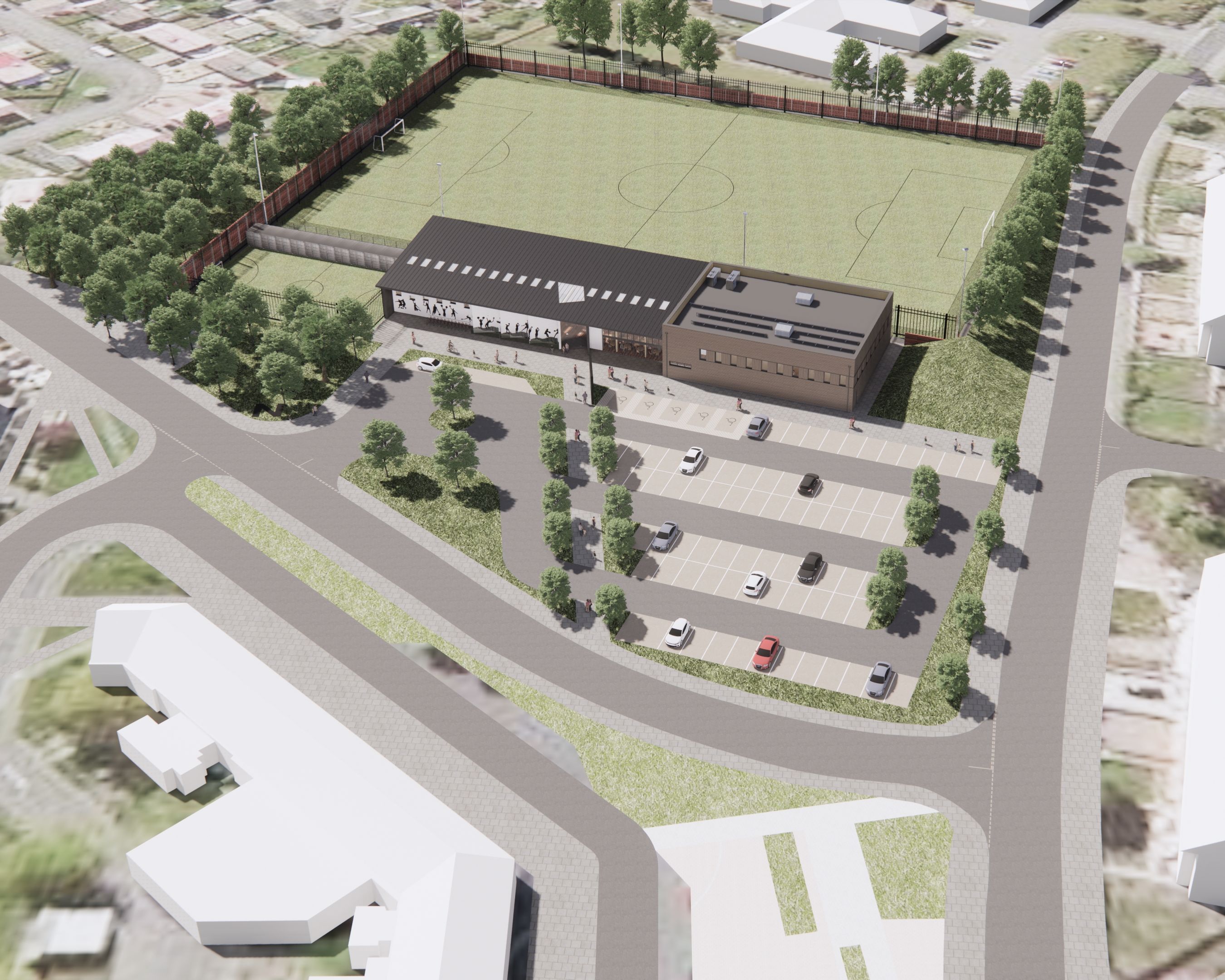 Aerial view of a sports complex with a soccer field, parking lot, and surrounding roads and buildings.