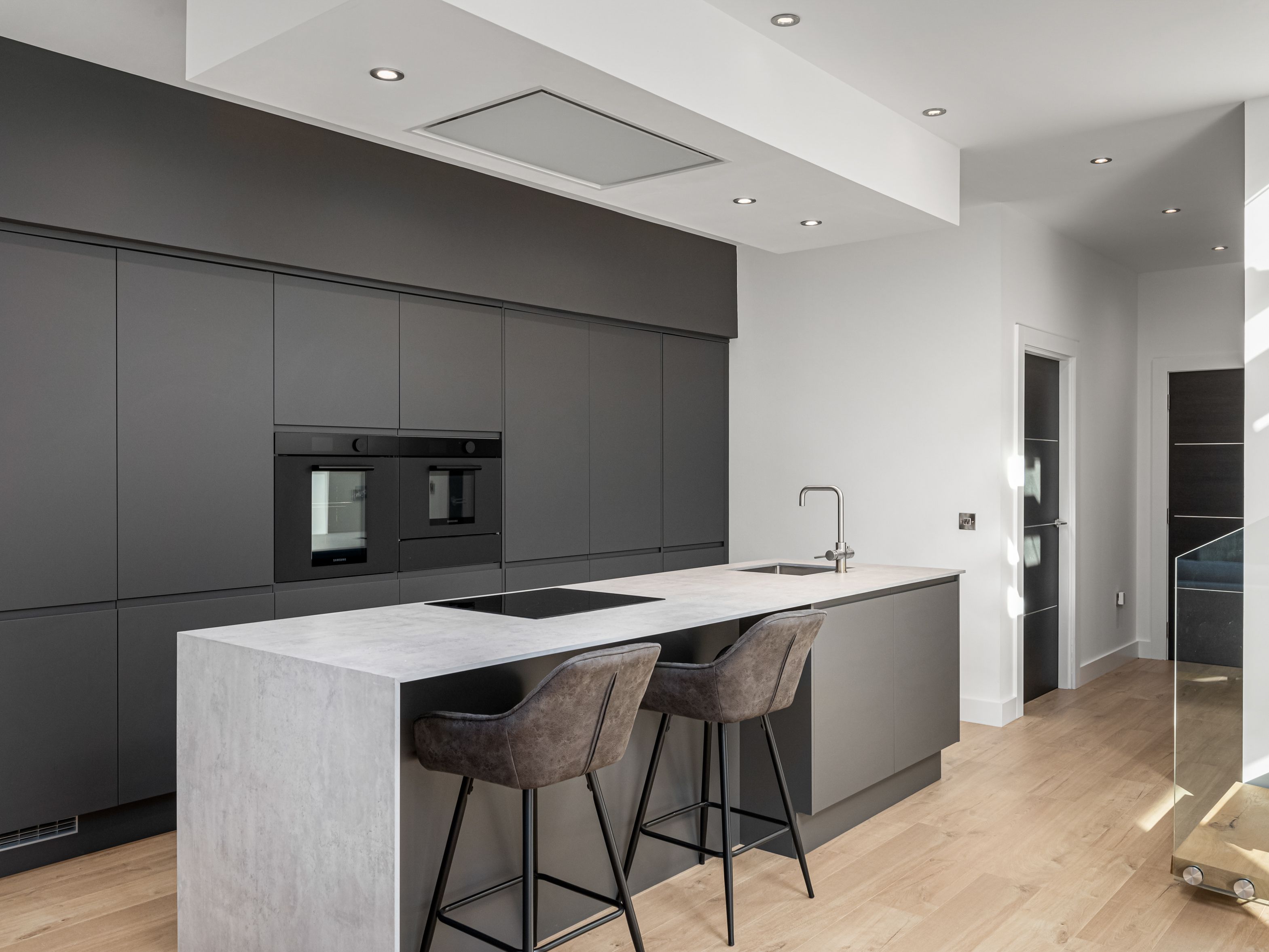 Modern minimalist kitchen with dark cabinetry, light wood flooring, and a marble island with two bar stools