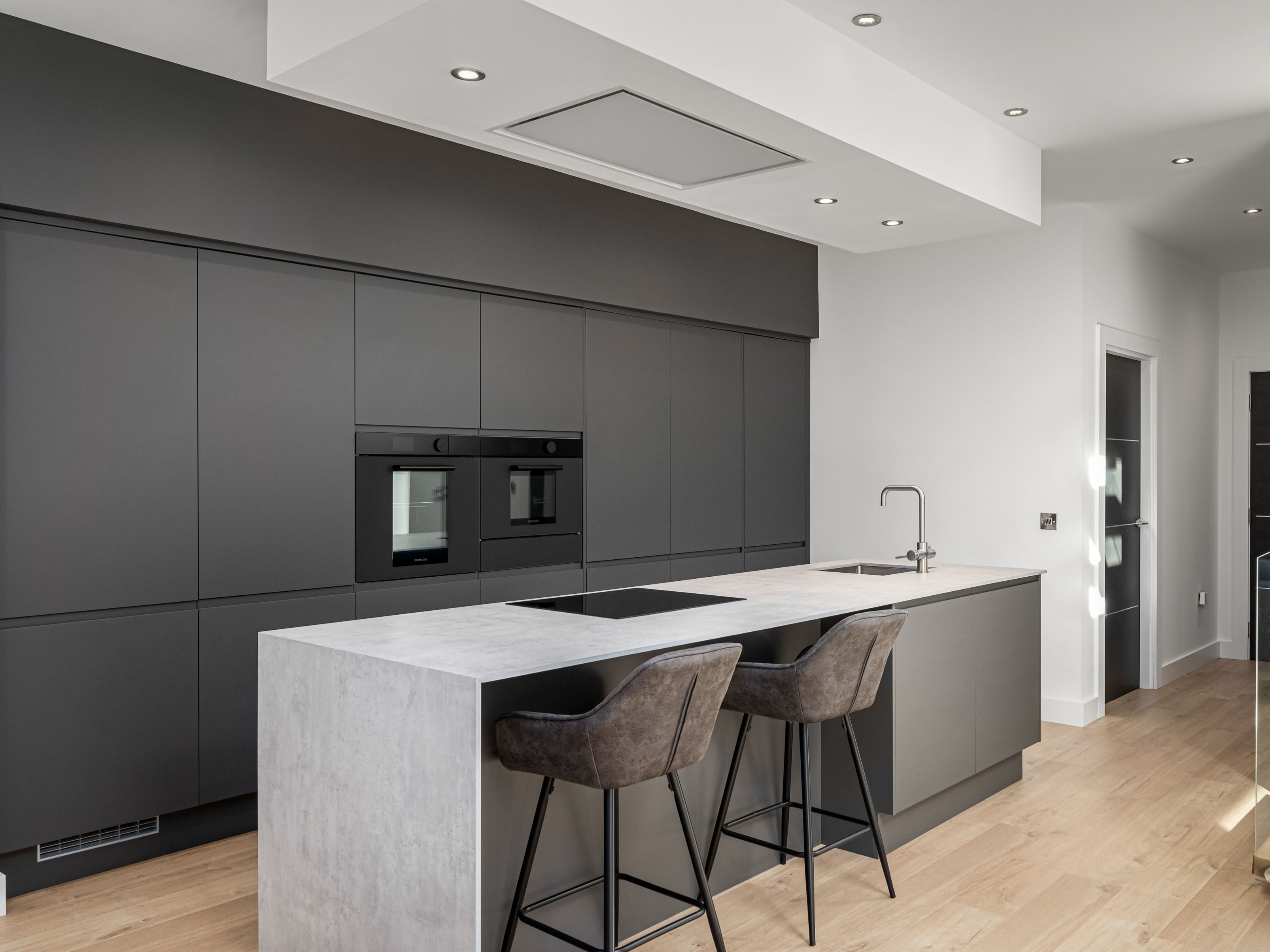 Modern minimalist kitchen with dark cabinetry, light wood flooring, and a marble island with two bar stools