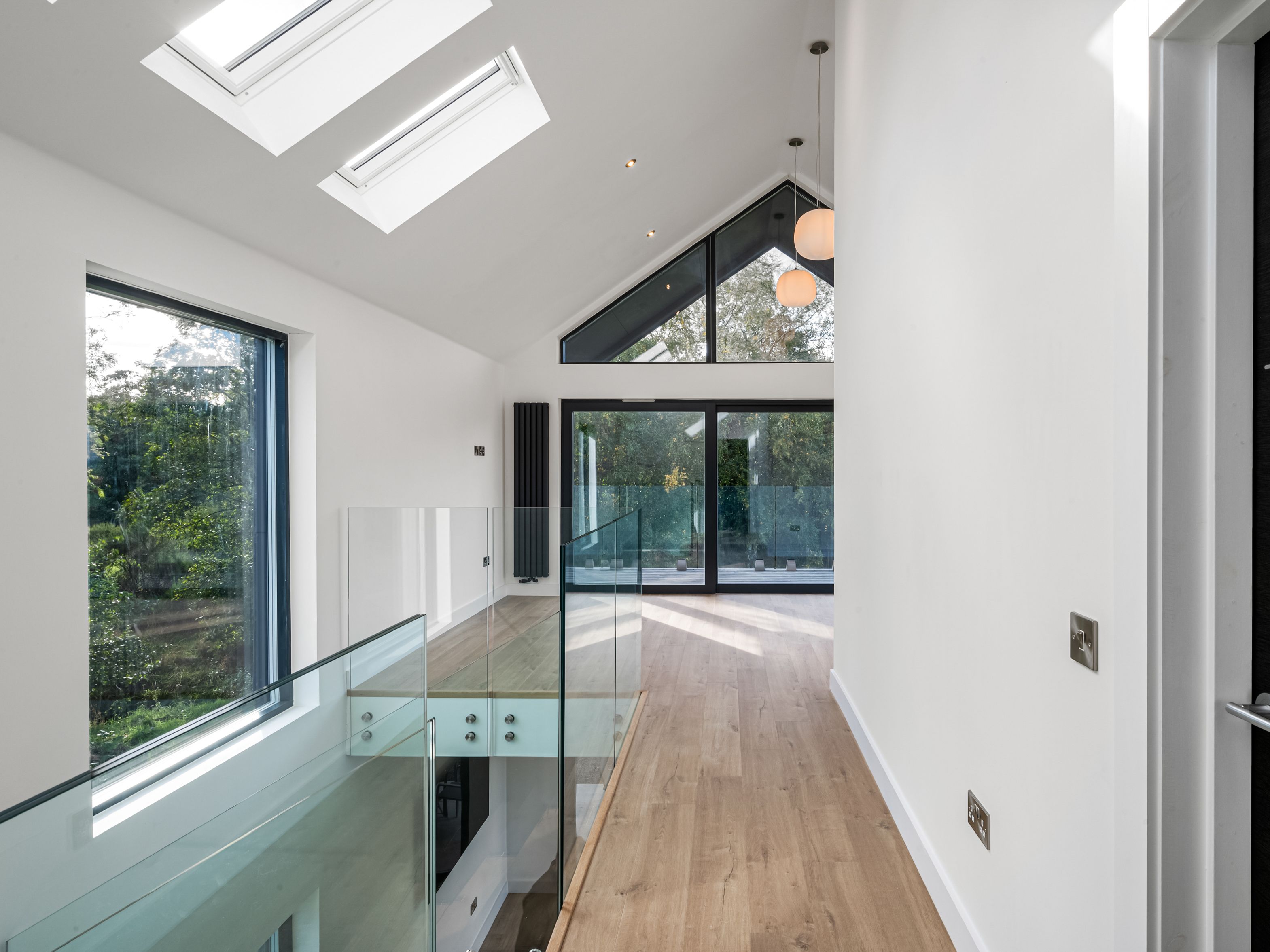 Modern hallway with glass balustrade, wooden floor, skylights, and large windows.