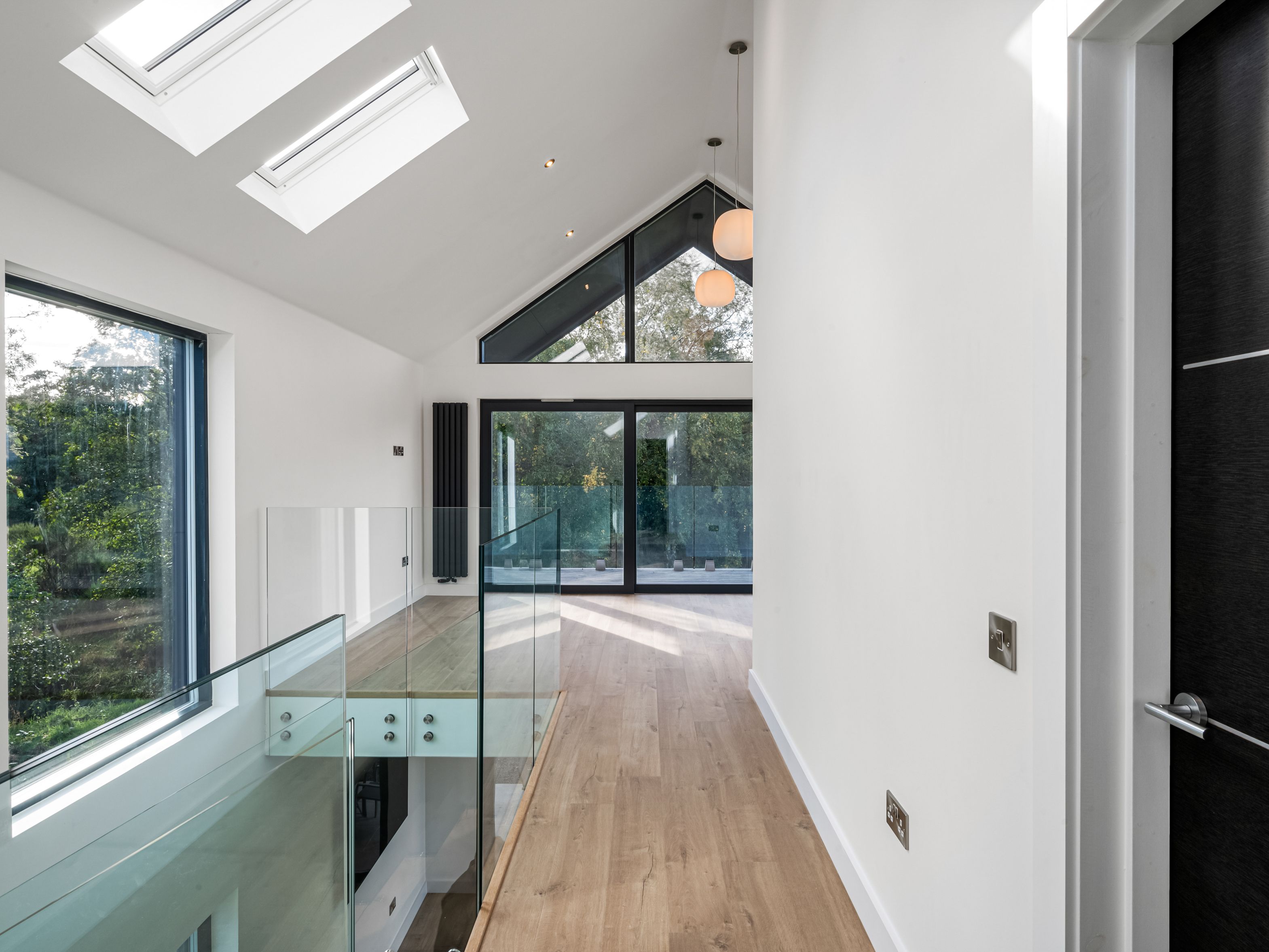 Modern hallway with glass balustrade, wooden floor, skylights, and large windows.